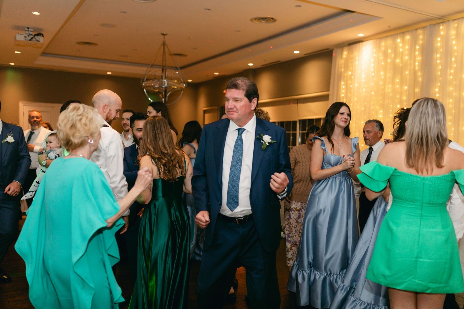 Wedding guests dancing and mingling at reception with green and blue attire.