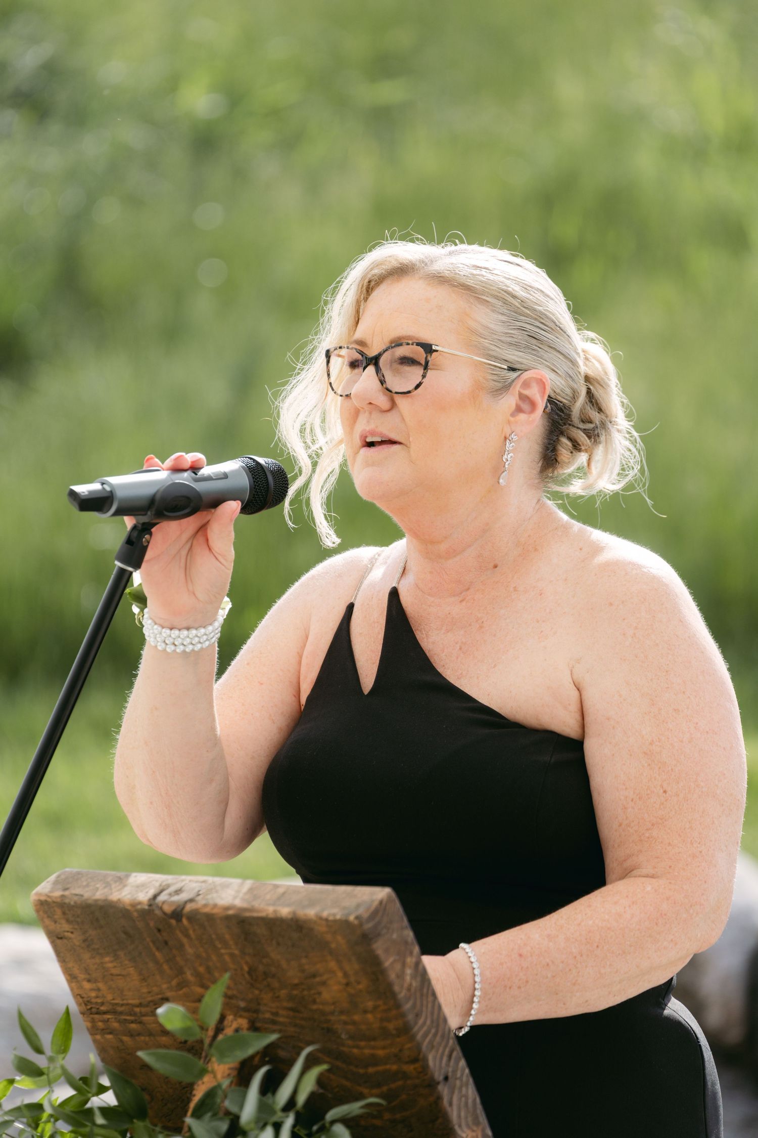 Singer performs passionately at an outdoor wedding venue with greenery in background.