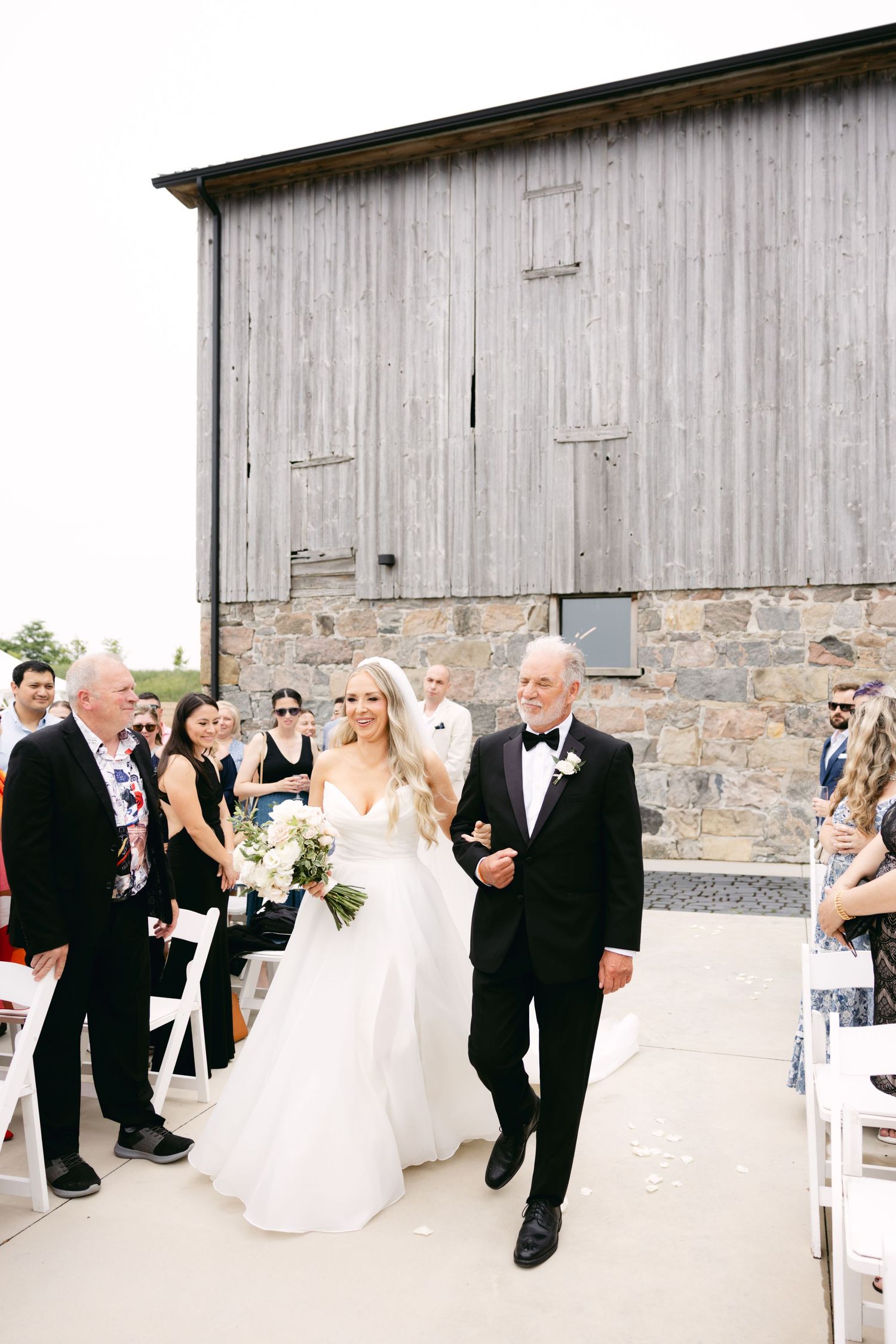 Wedding party walking along stone building during outdoor celebration.