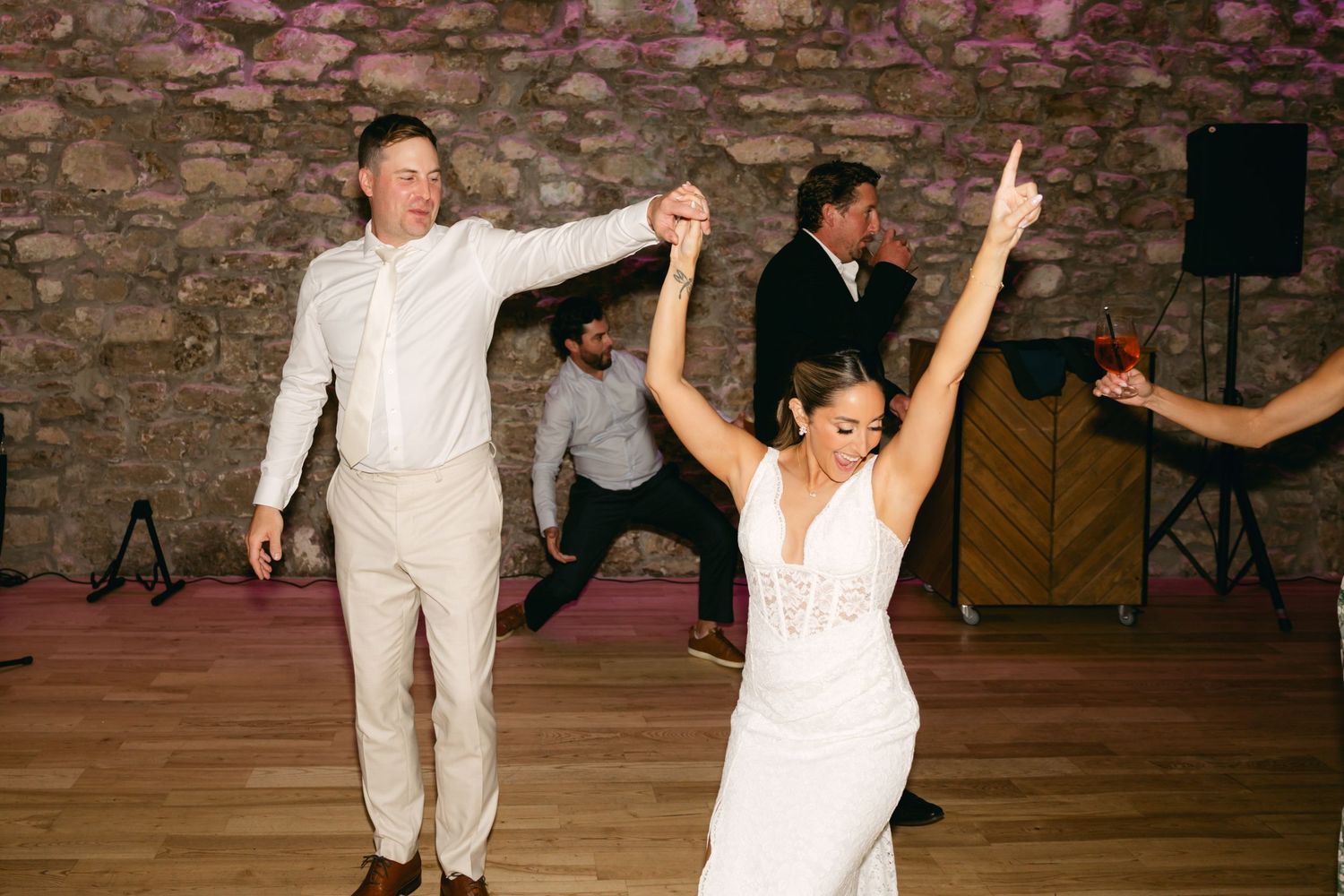 Dancers perform energetic moves on a dance floor with stone walls and purple lighting.