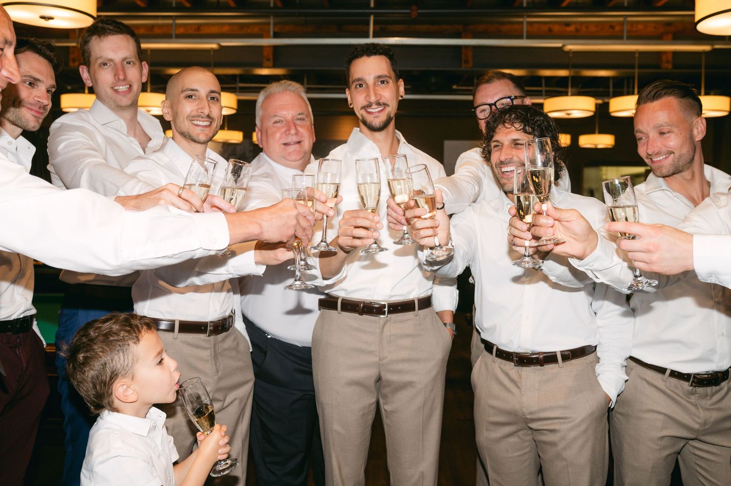 Groomsmen in beige suits raising glasses for a celebratory toast.
