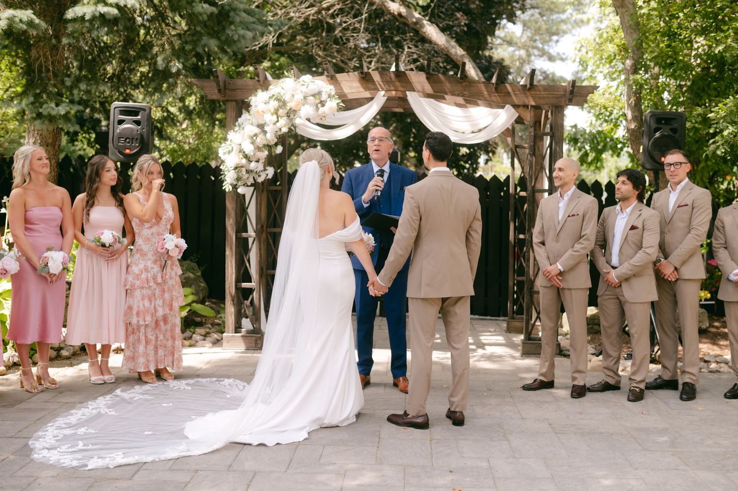 Wedding party members line up for photos outdoors with pink and tan color scheme.