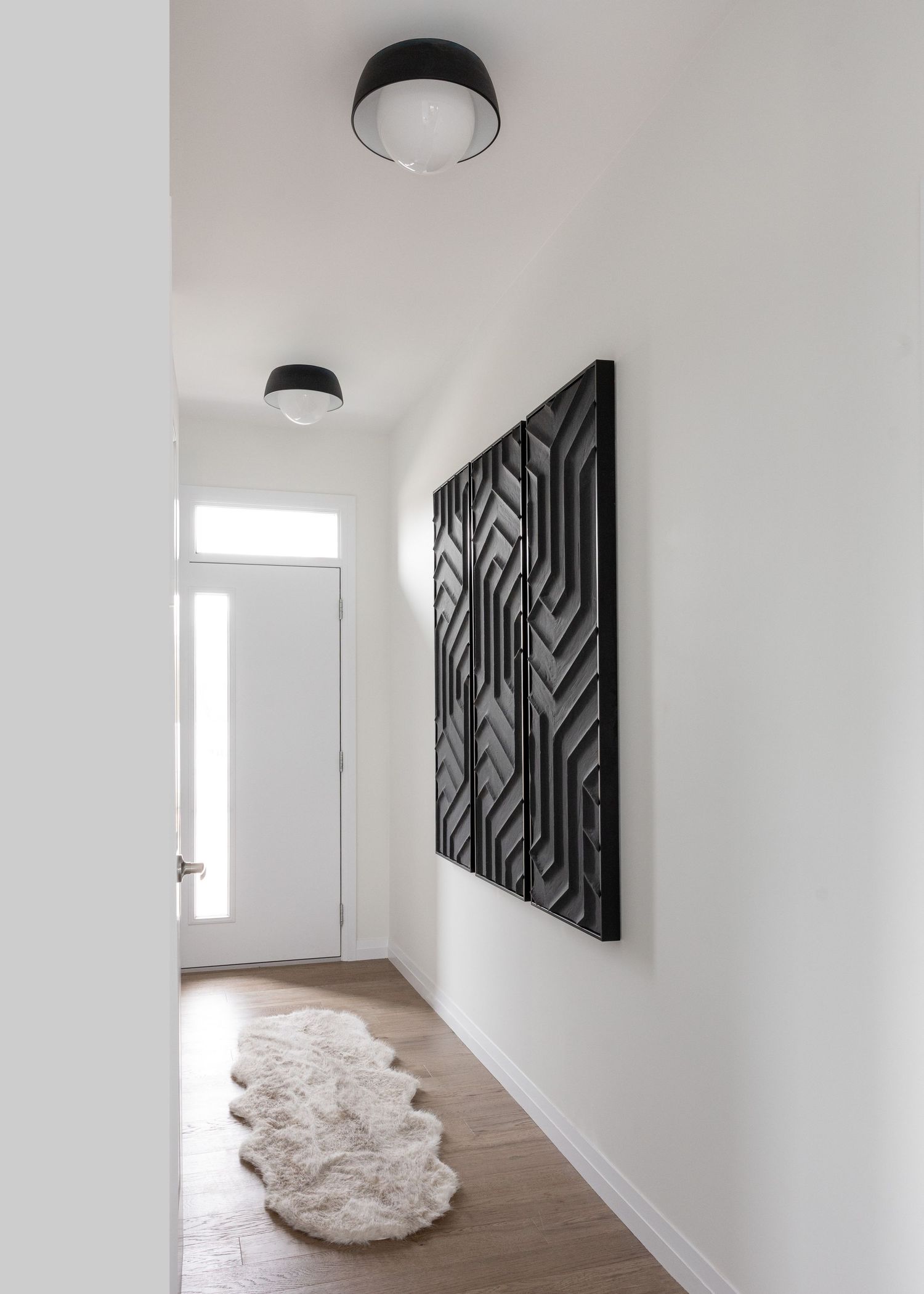 Modern hallway with geometric black wall art and natural light from tall windows.