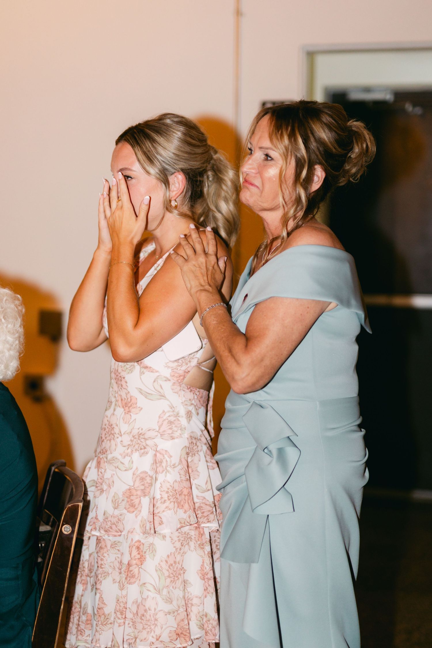 Emotional wedding moment captured as guests share tears and hugs in light blue dresses.