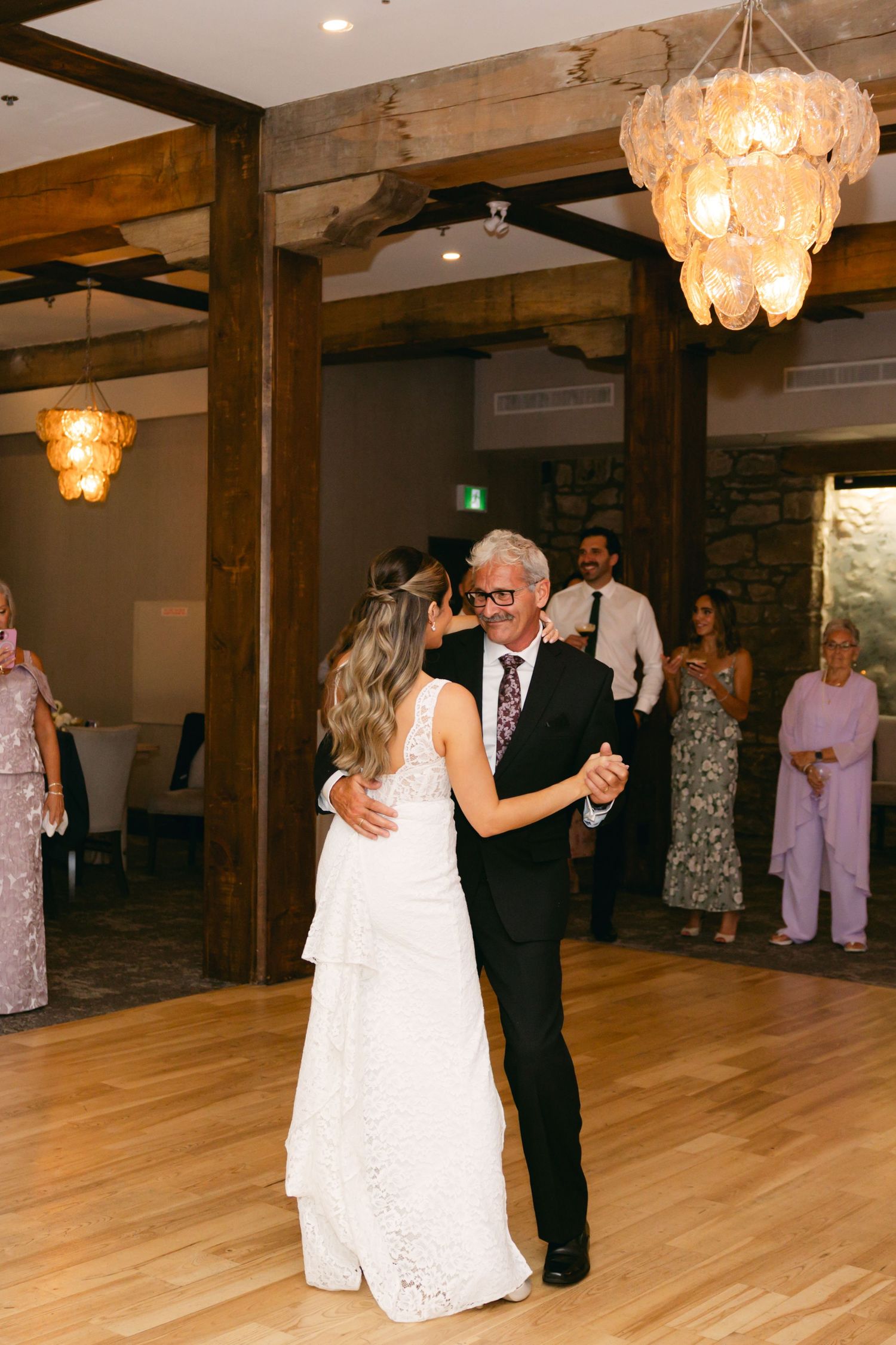 Couples slow dancing at an elegant reception venue with exposed beams and stone walls.