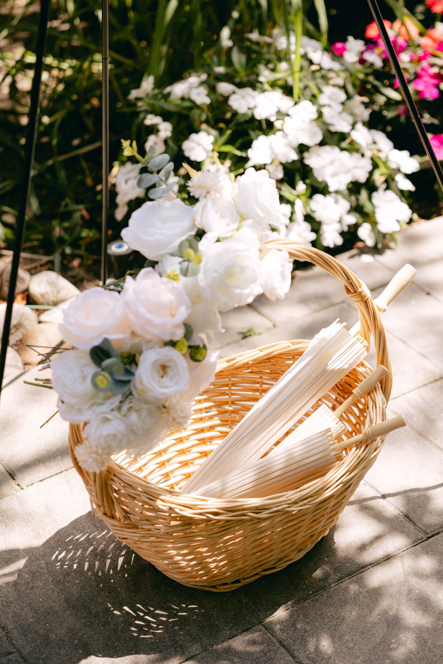 A wicker basket with white roses and wedding decor on a stone patio surrounded by flowers.