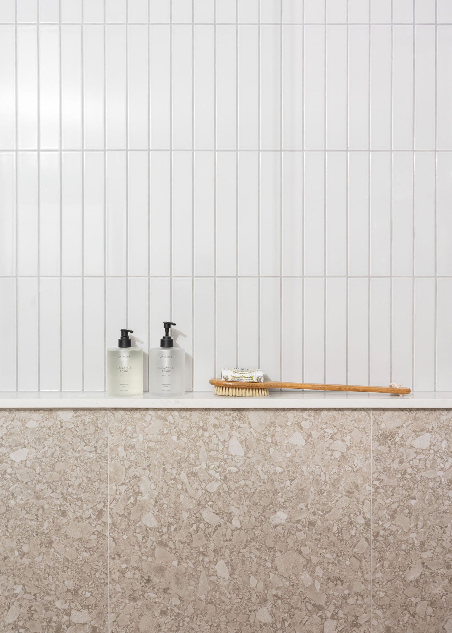 White vertical tile backsplash with terrazzo-style counter featuring bathroom accessories.