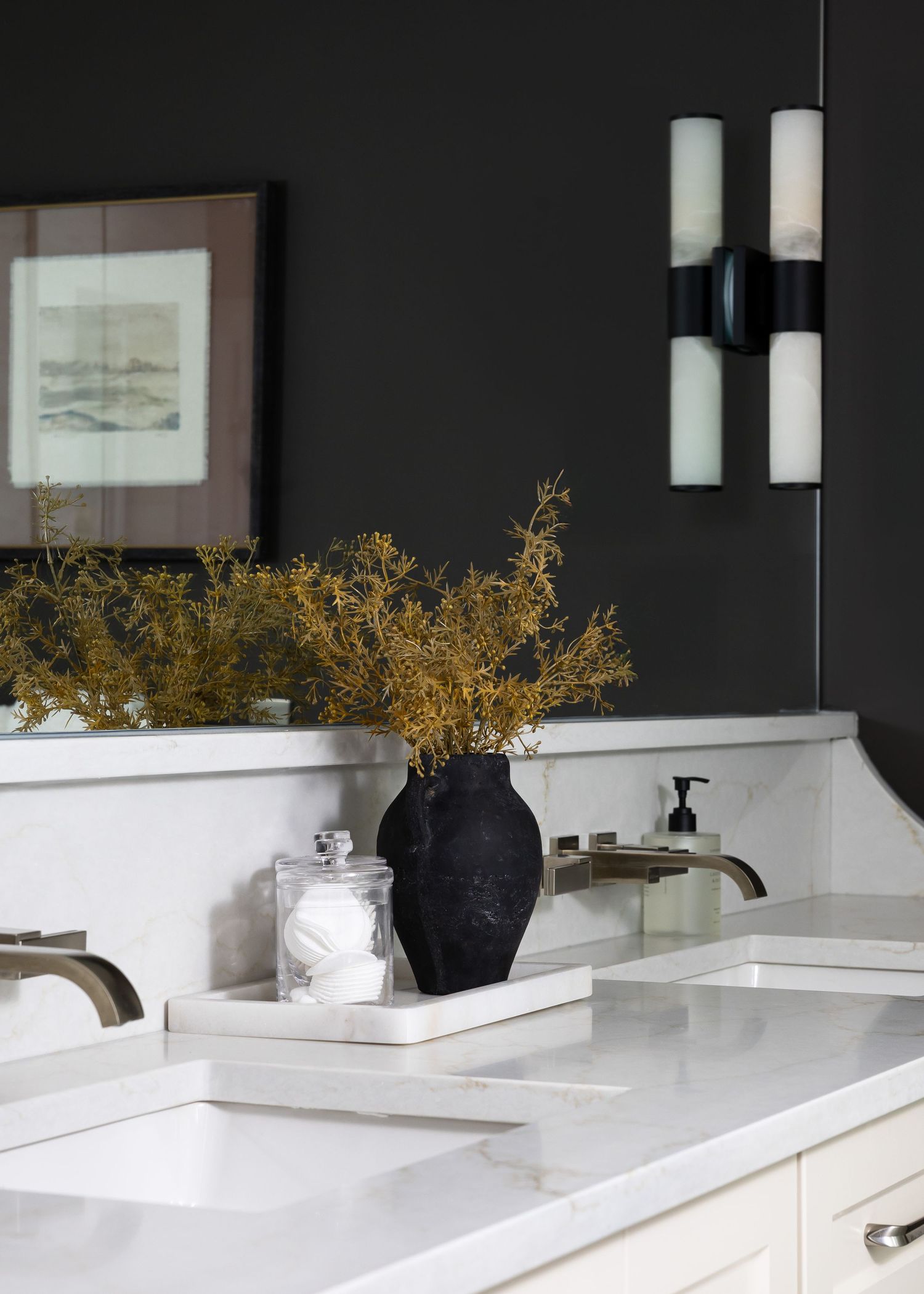 Contemporary bathroom vanity with black accent wall, white countertops, and decorative gold floral arrangements.