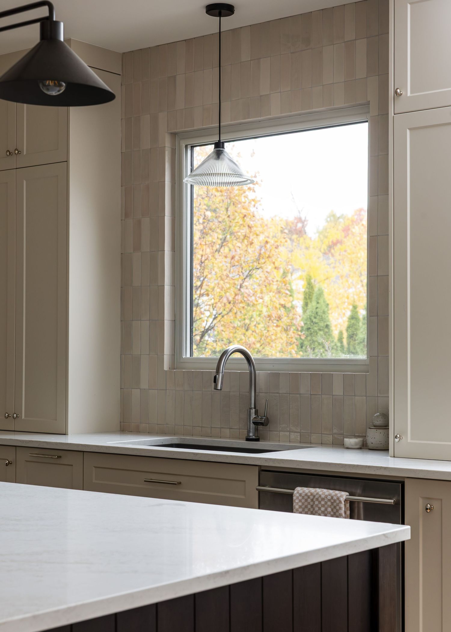 Bright kitchen with white quartz countertops and large windows overlooking autumn foliage.