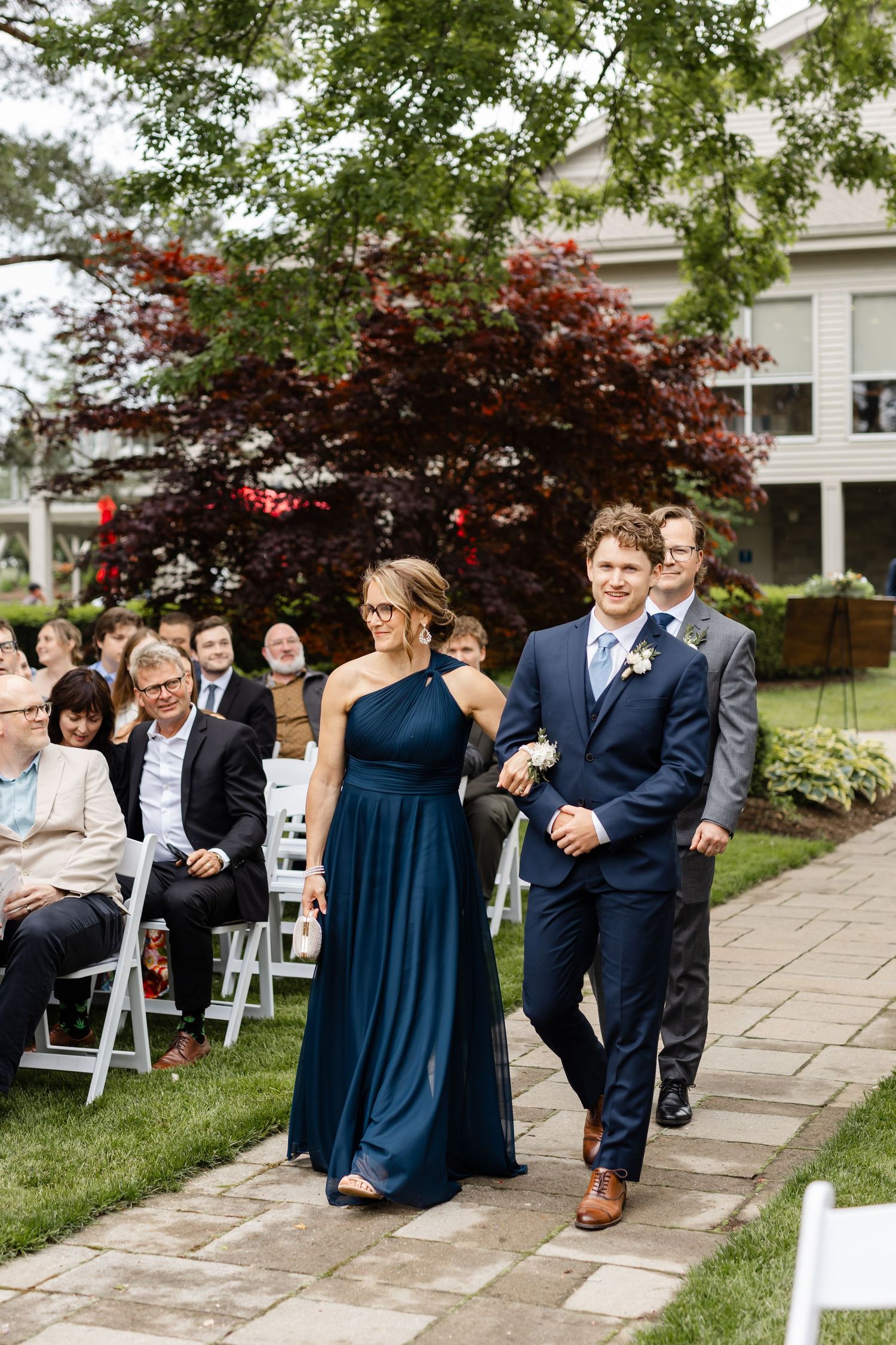 Wedding party members process down a stone pathway during an outdoor ceremony.