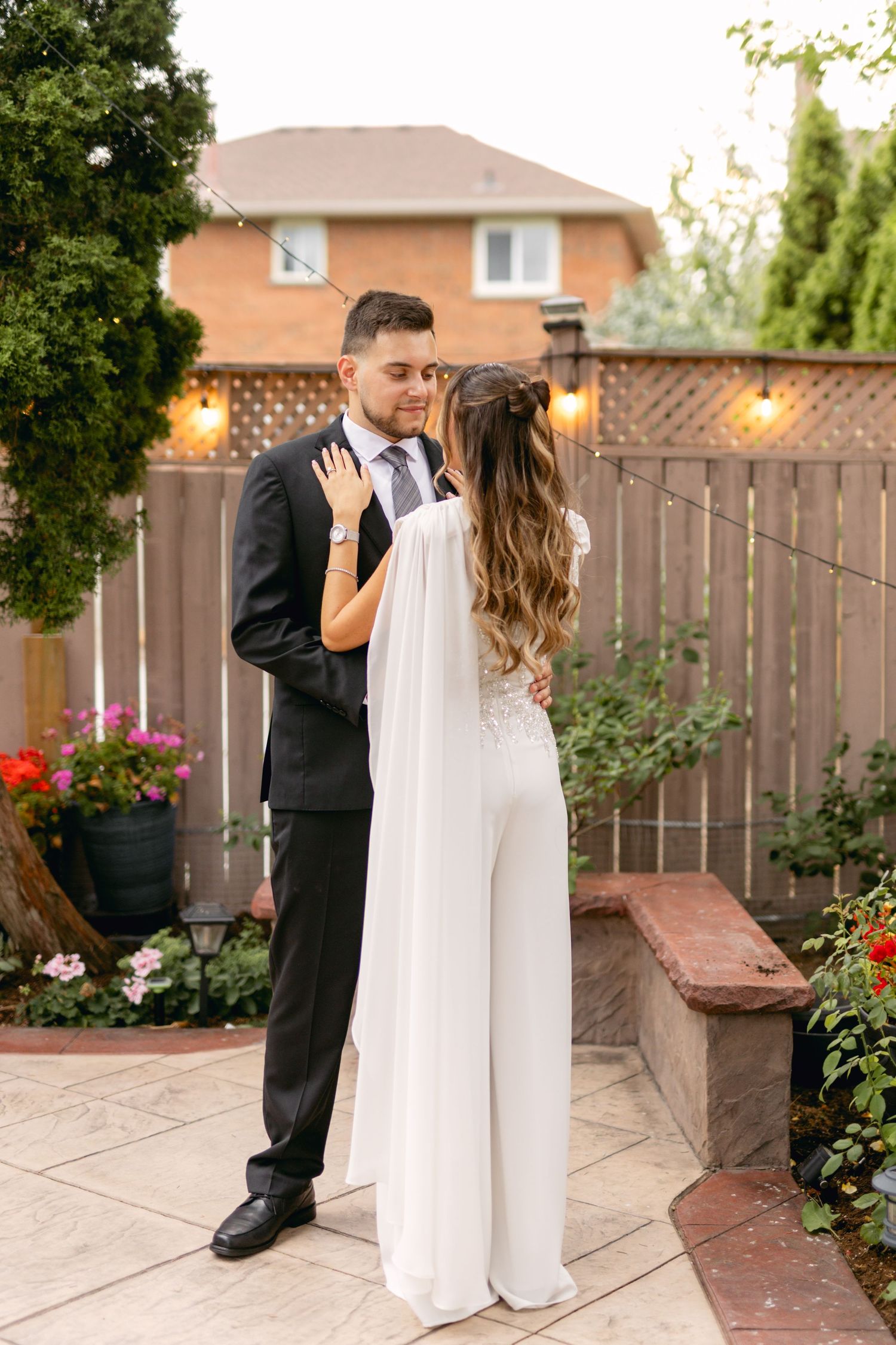 Romantic wedding portrait in backyard garden with string lights and wooden fence.