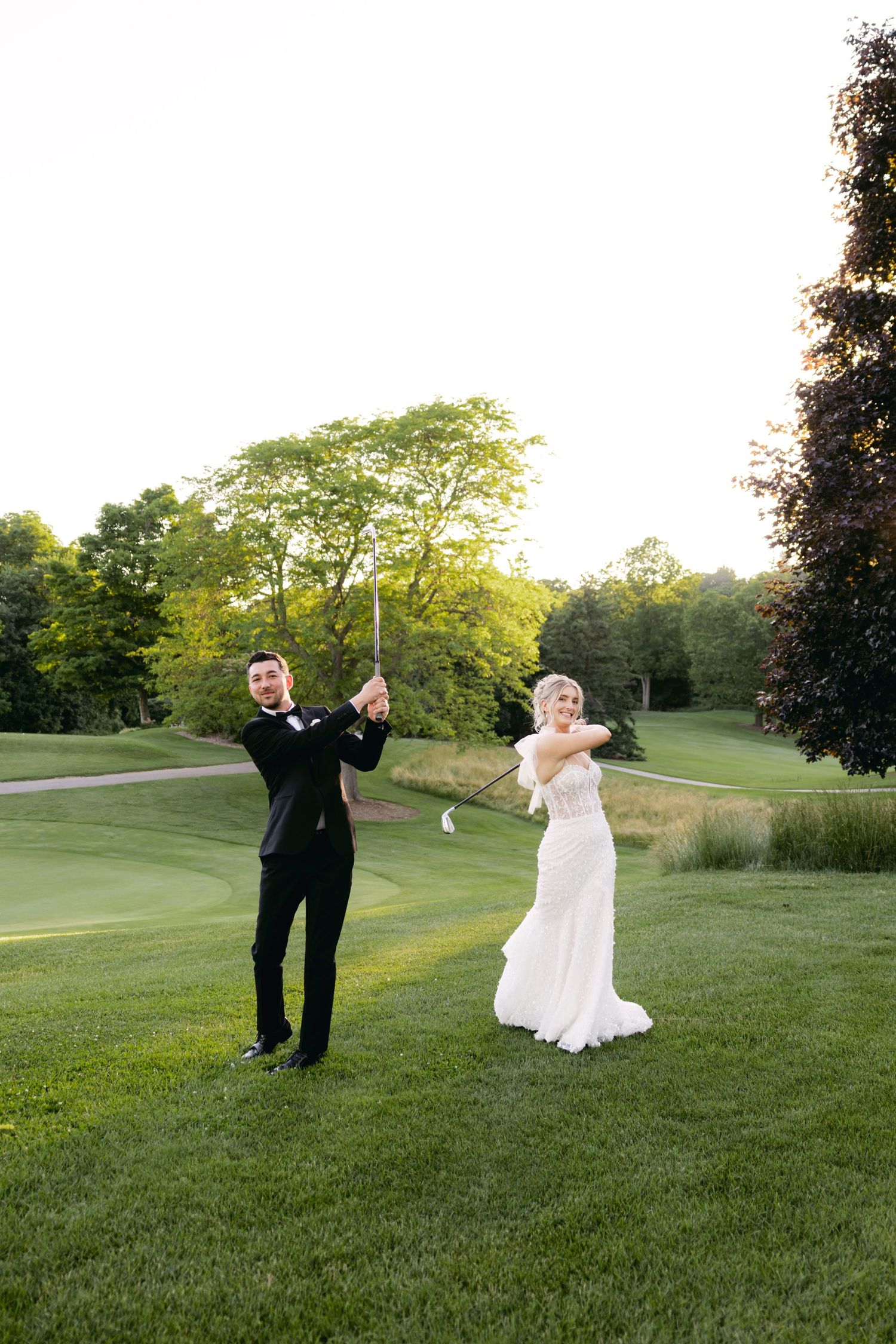 Wedding couple dances playfully on a grassy hill during golden hour.