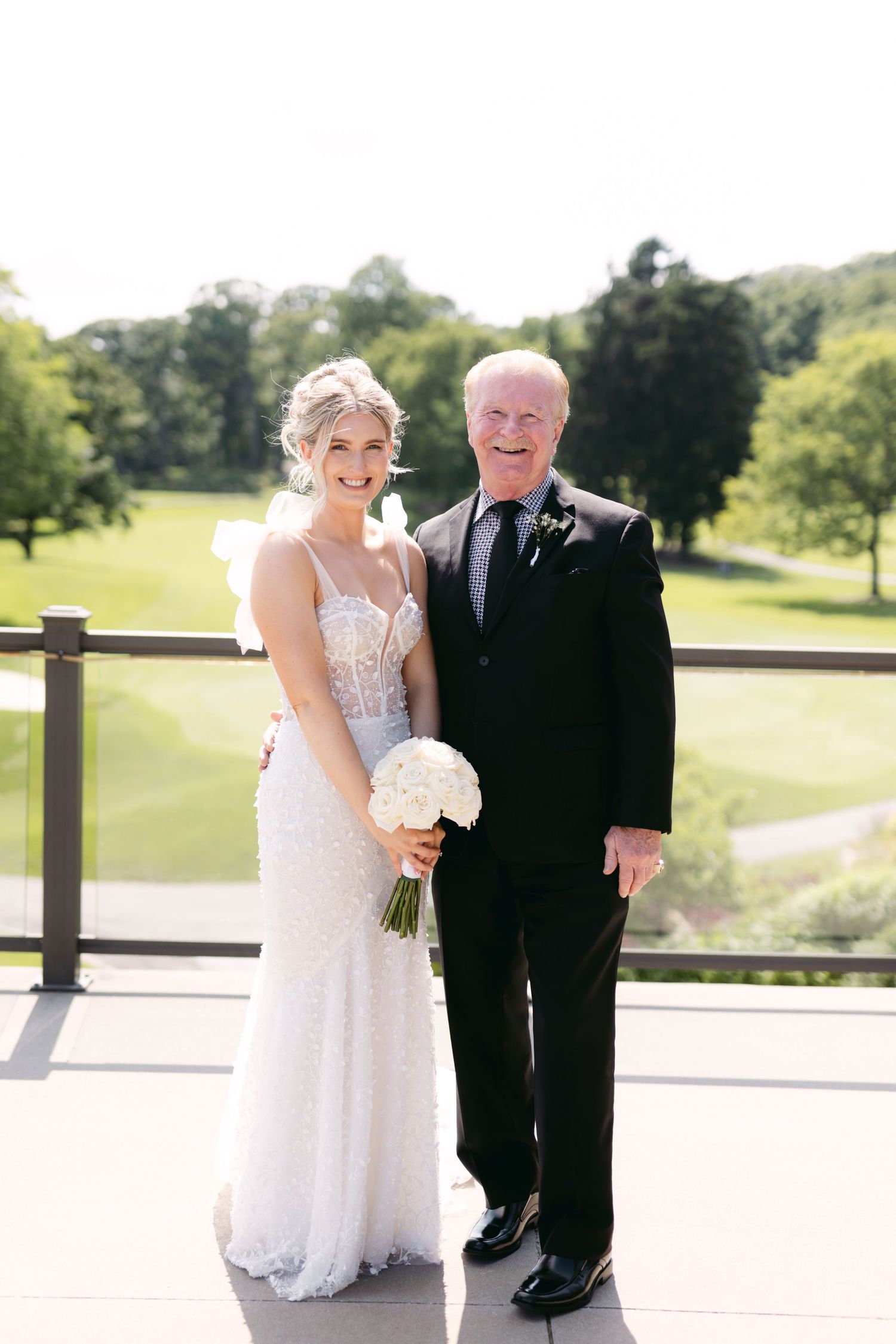 Wedding party members pose together on a sunny patio overlooking a golf course.