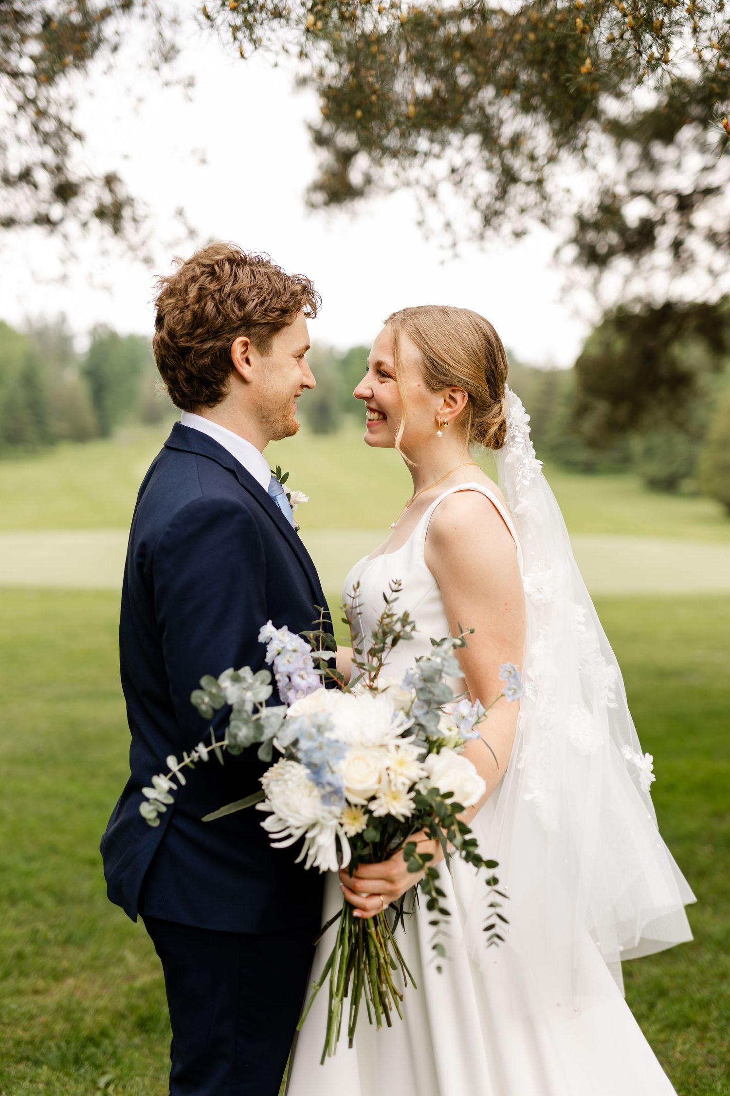 Wedding couple poses with an elegant white bouquet in a scenic outdoor setting.