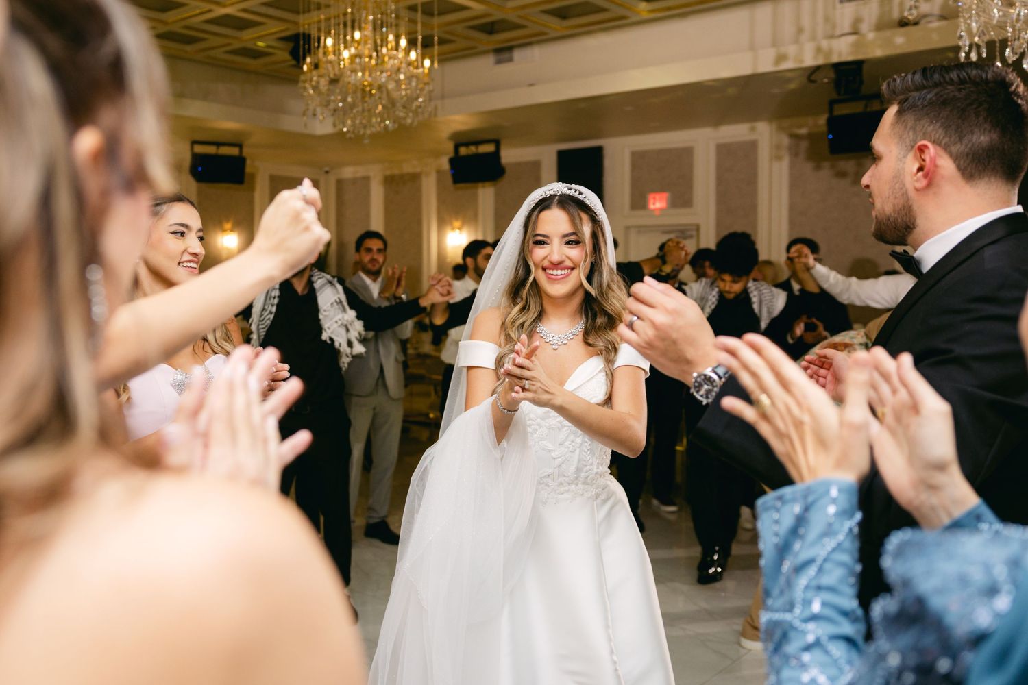 Wedding celebration with guests dancing and clapping in an ornate reception venue.