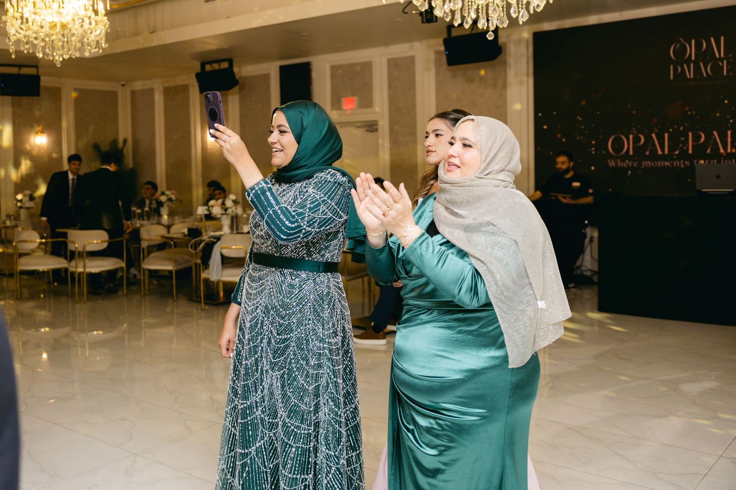 Two guests in elegant formal wear dance and celebrate at a wedding reception.