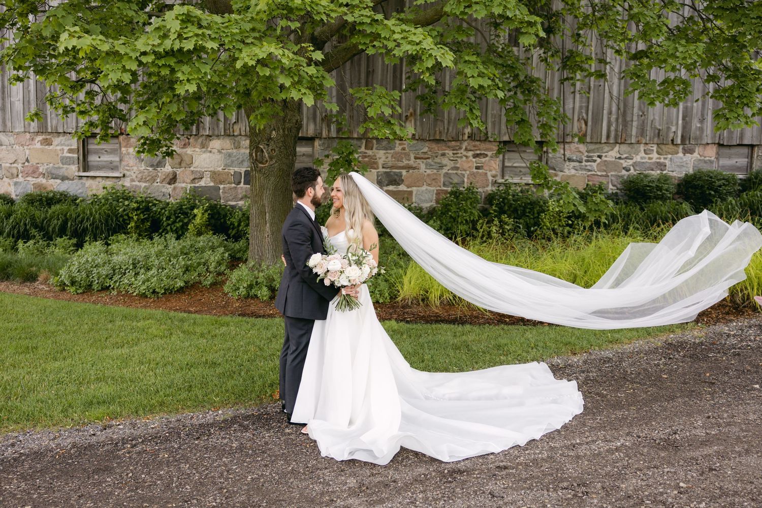 A romantic wedding portrait with the bride's veil flowing dramatically in the breeze on a garden path.