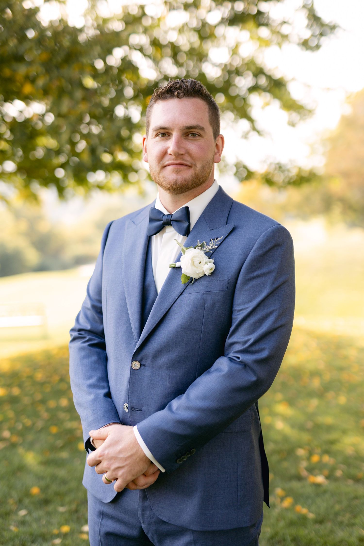 Groom in navy blue suit with boutonniere poses outdoors on wedding day.