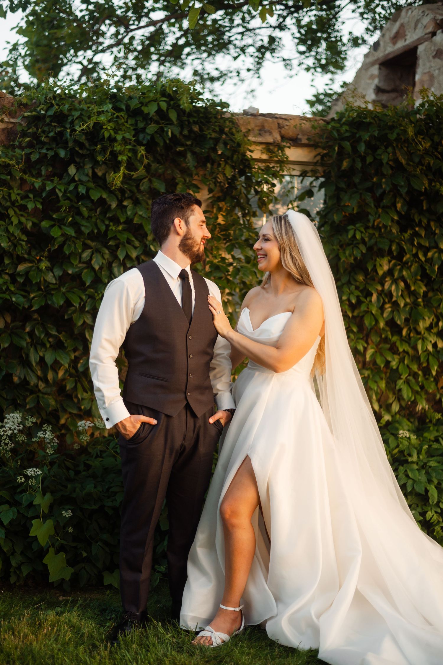 Wedding couple poses playfully against a backdrop of green foliage.