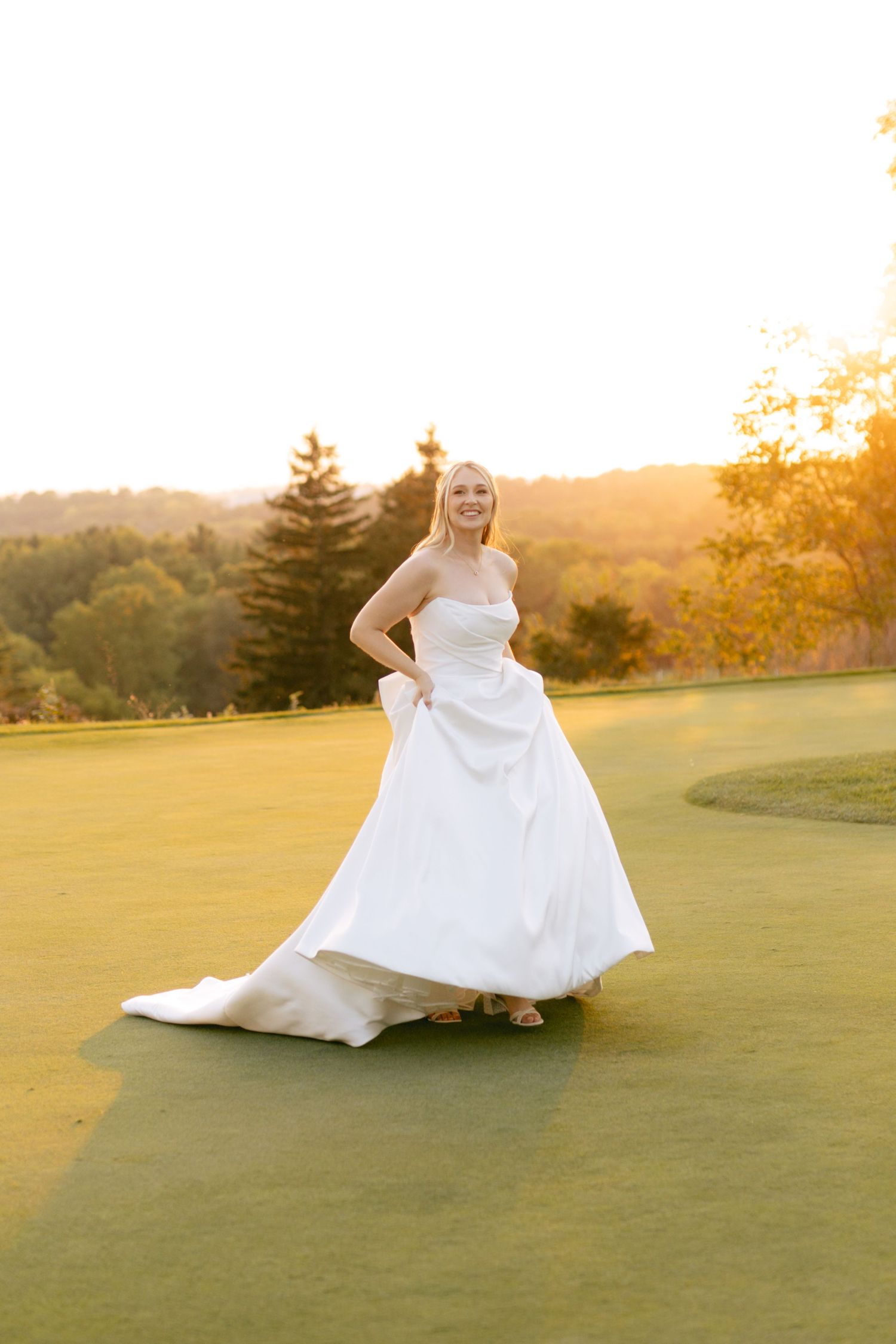 Bride in elegant white gown poses on golf course during golden hour photography session.