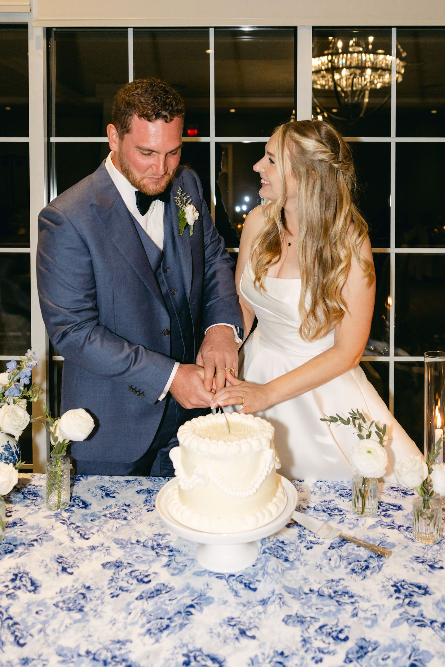 Wedding couple cuts their cake together at reception with blue and white table decor.