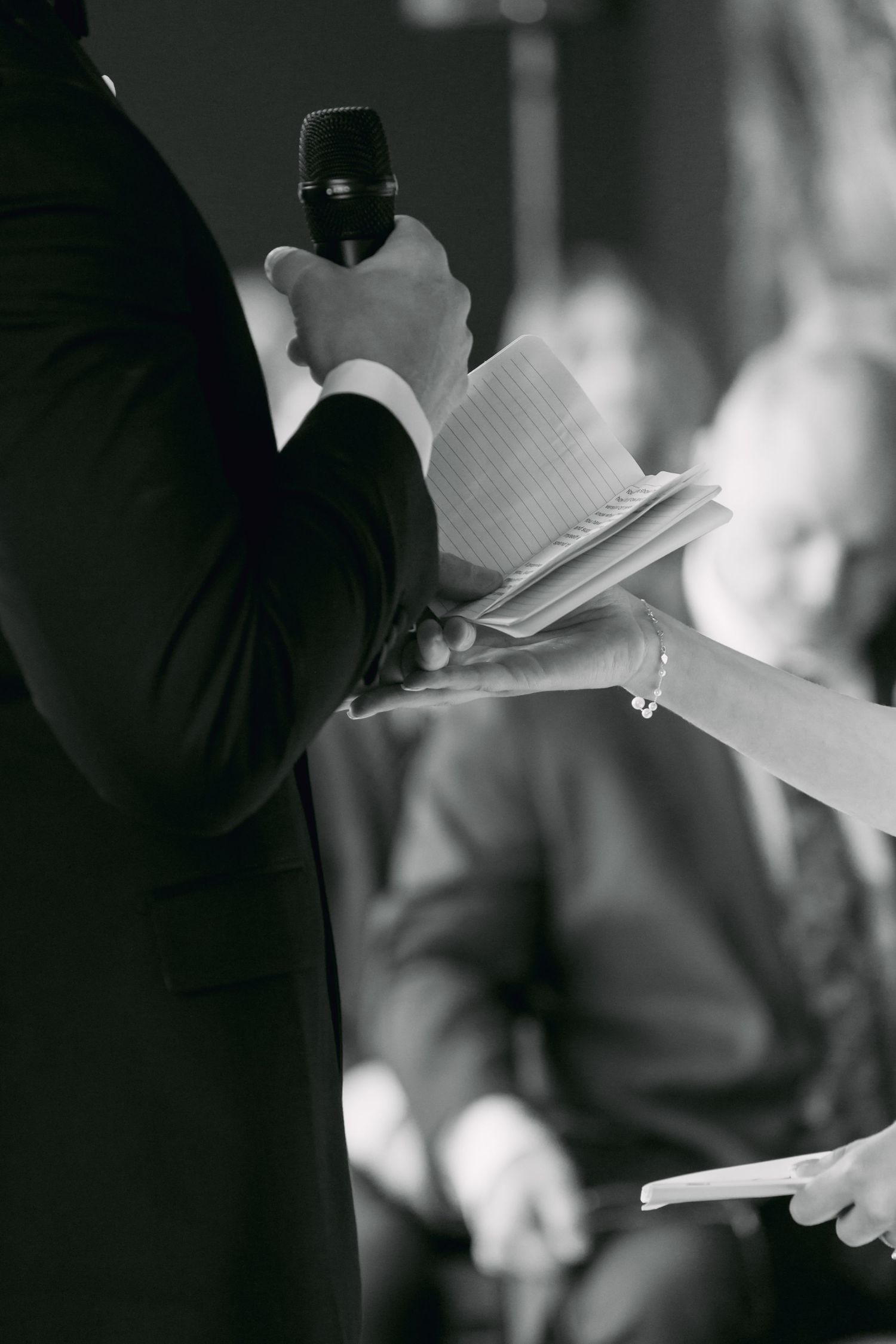 Black and white photo of officiant holding microphone and notes during an intimate wedding ceremony.