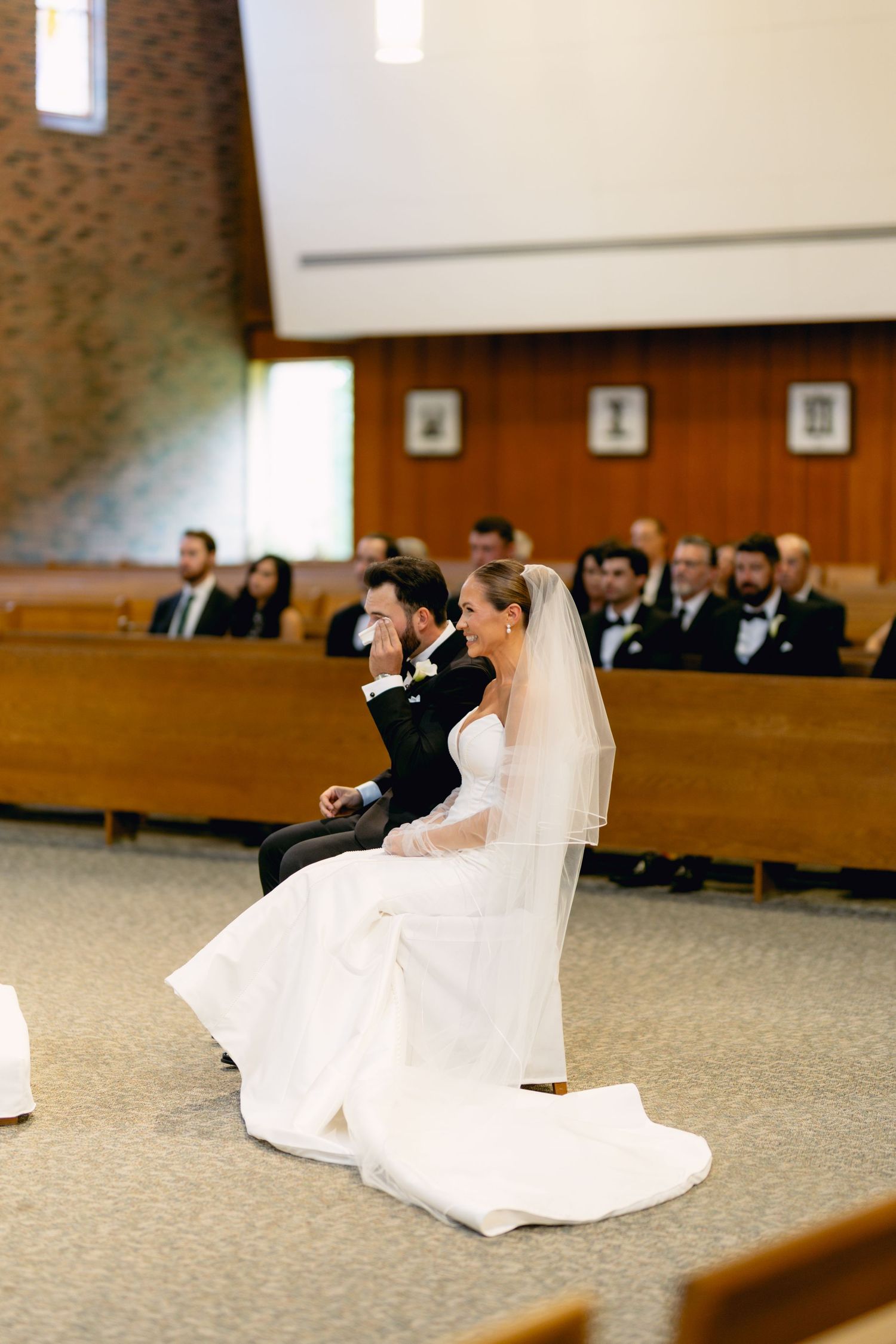 Bride and groom seated at church altar during wedding ceremony with guests in pews behind them.