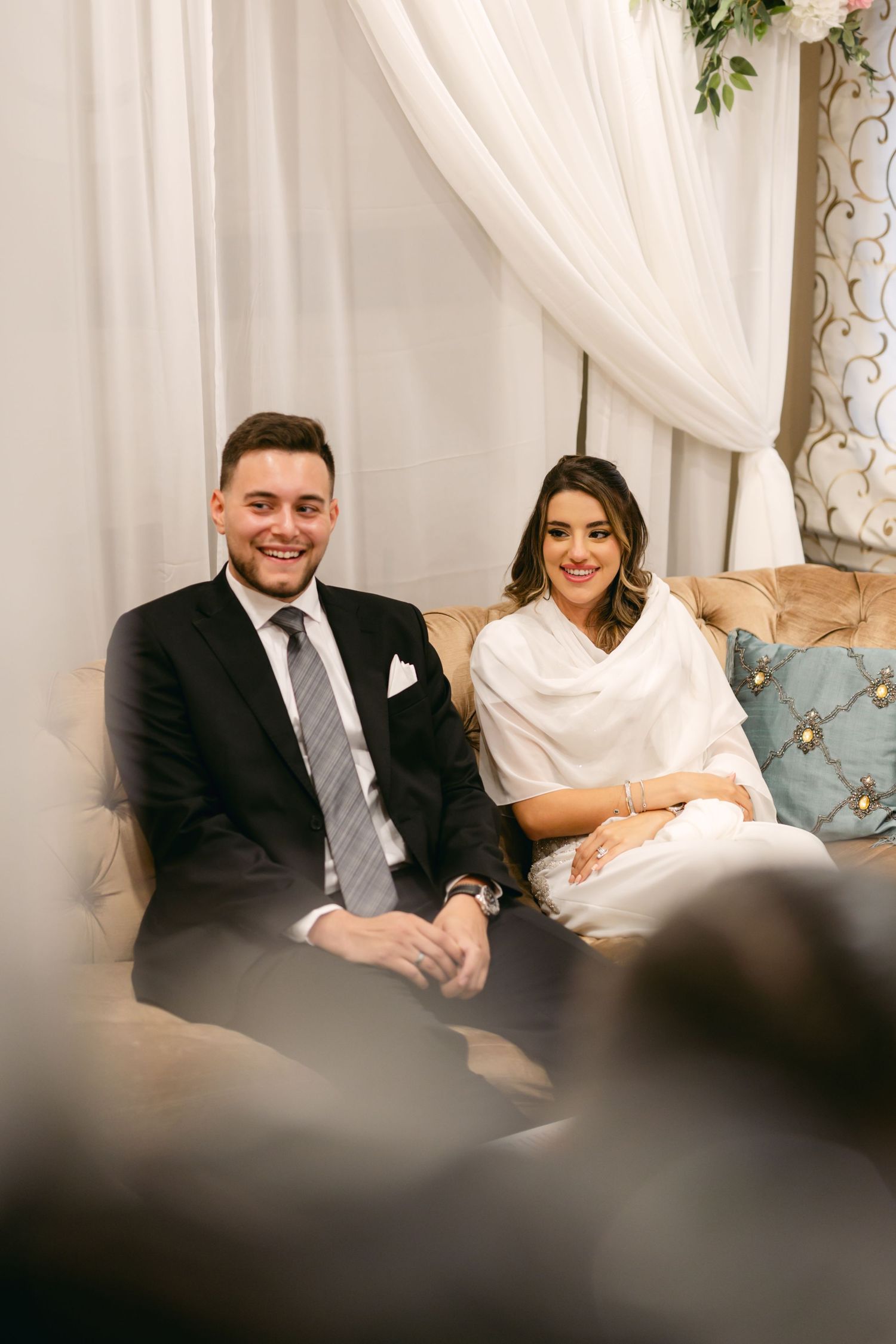 A couple sits together on an elegant couch during their wedding ceremony.