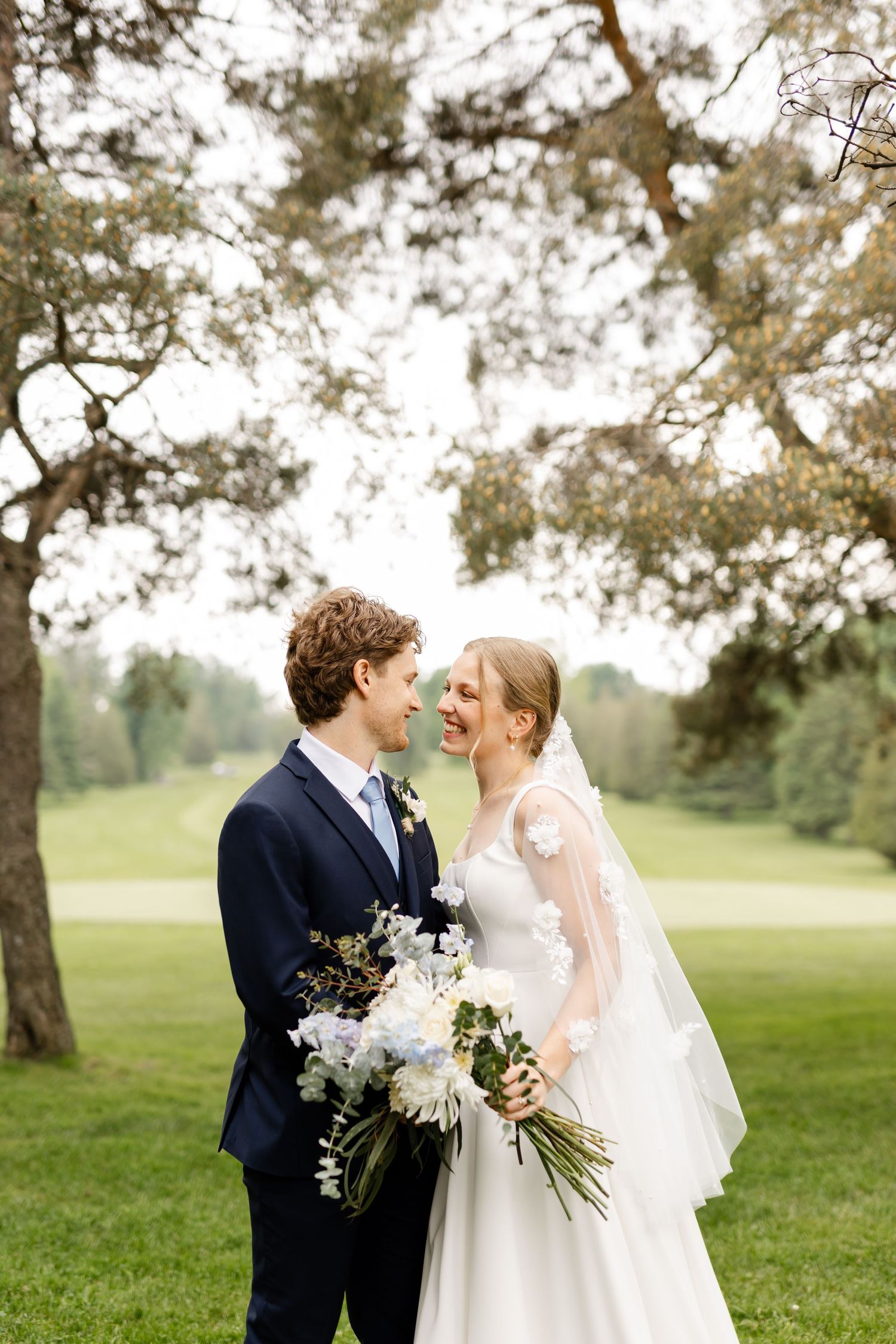 Elegant couple shares intimate moment on golf course holding white and green bouquet.