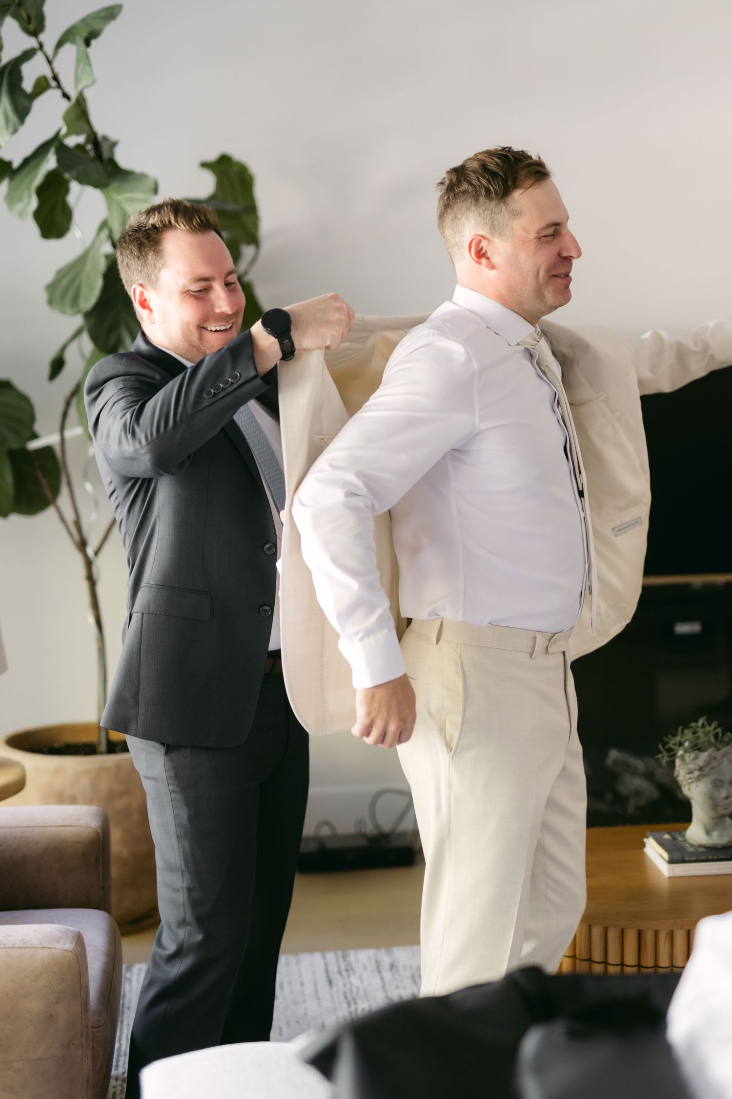 Groomsmen in formal attire assist each other with wedding day preparations.