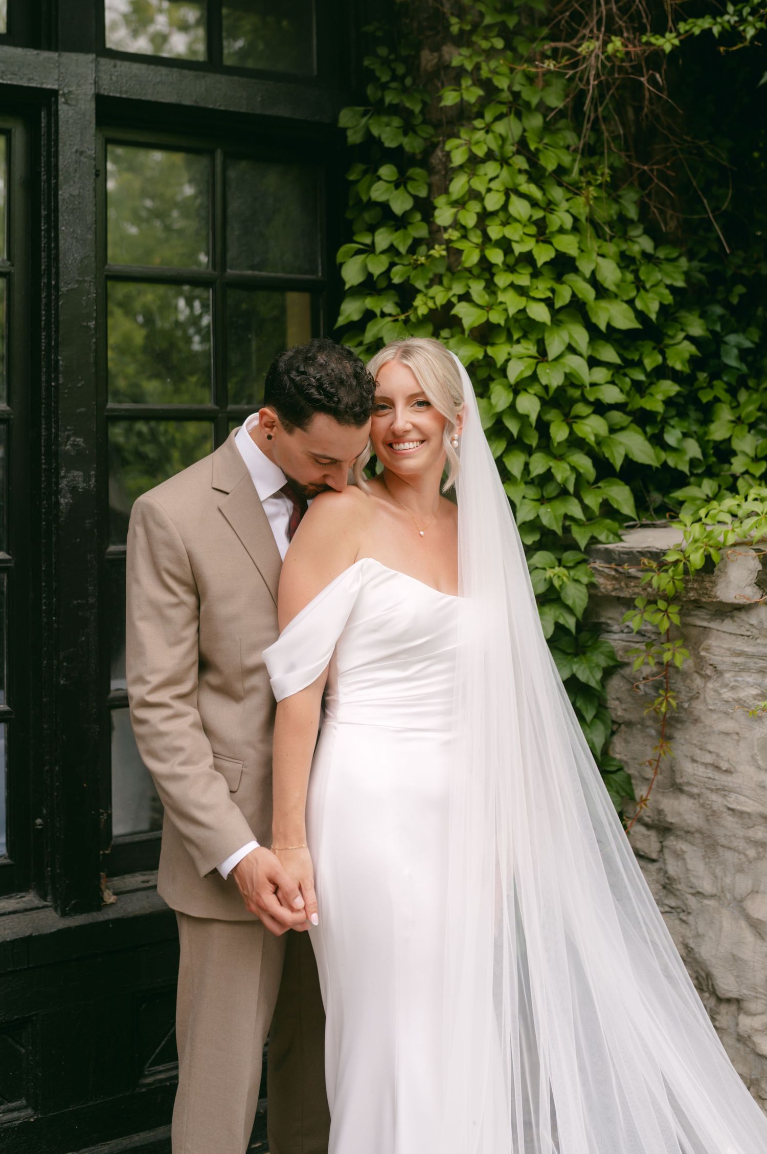 Intimate wedding moment shared between couple against ivy-covered stone wall.