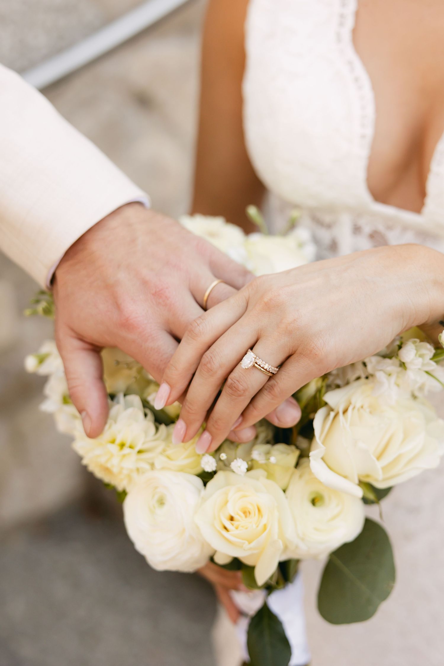 Close-up of hands holding a white rose bouquet with wedding rings visible.