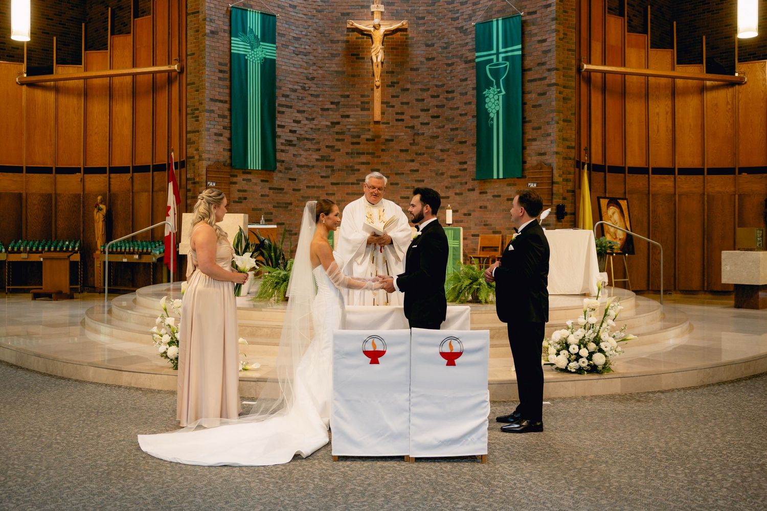 Catholic wedding ceremony at church altar with bride, groom, priest, and witnesses before a crucifix.