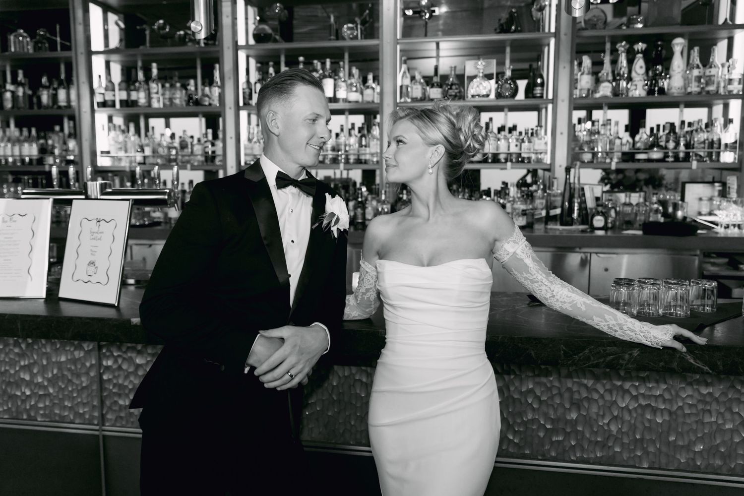 Bride and groom in black and white photo posing together at elegant bar setting.