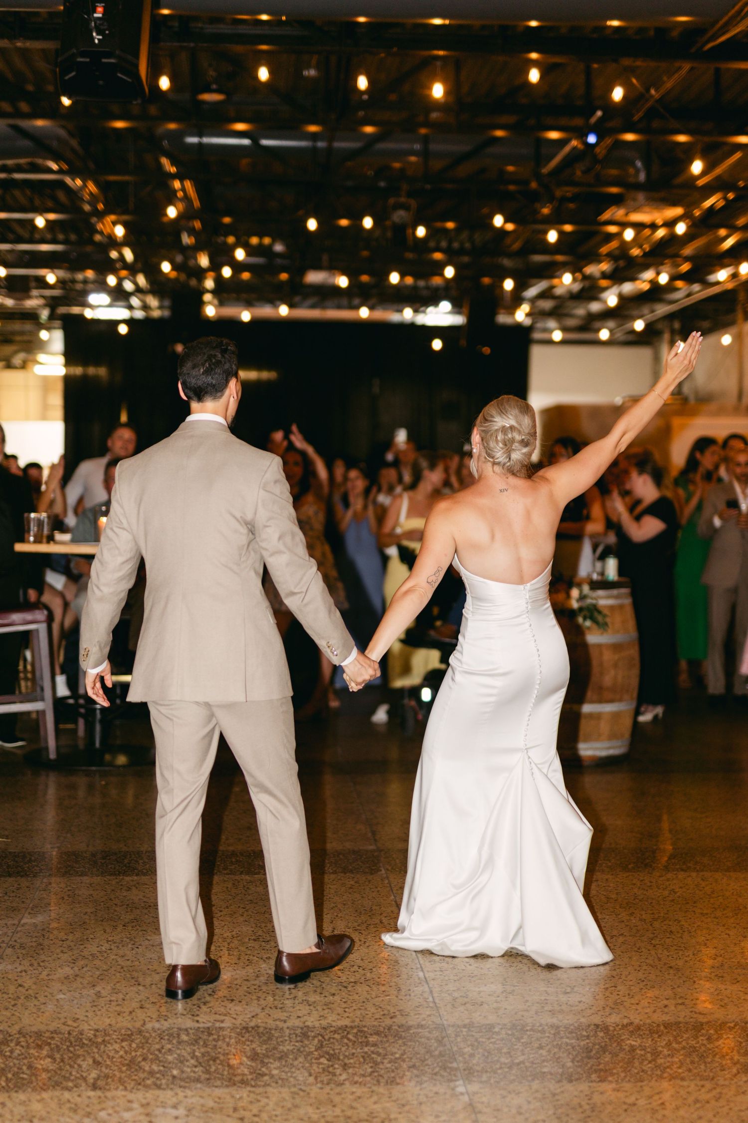 Wedding party dances together on polished floor under romantic string lights.