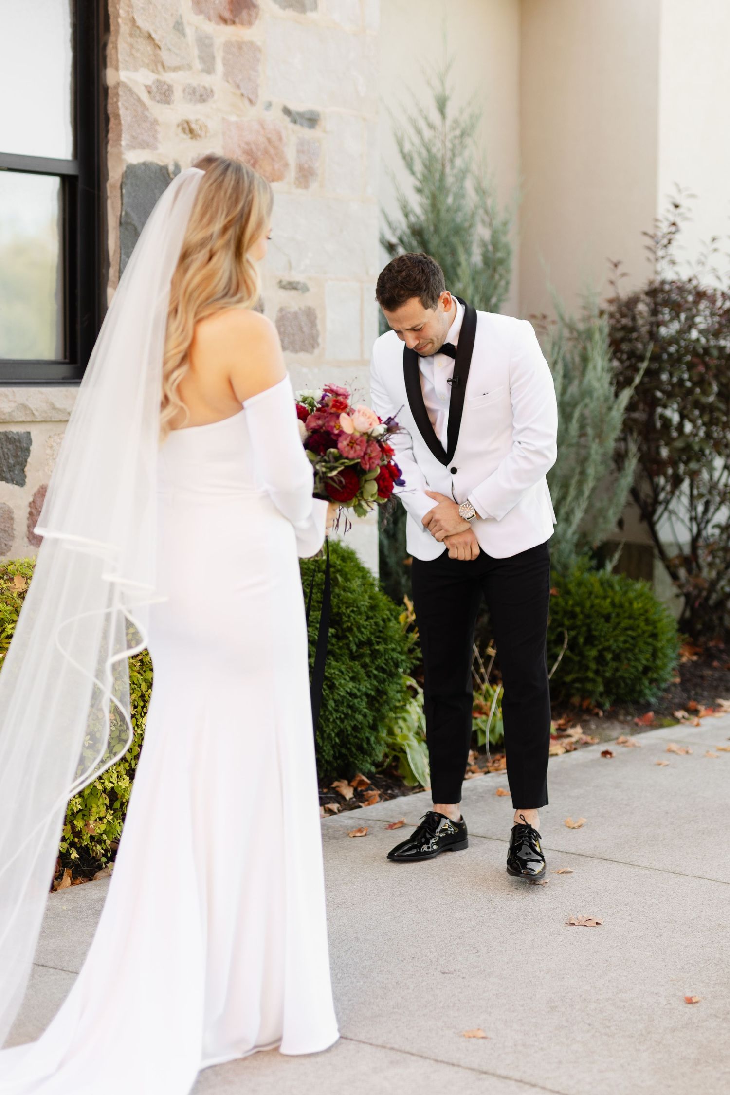 A bride in a flowing veil approaches her groom during an emotional first look moment.
