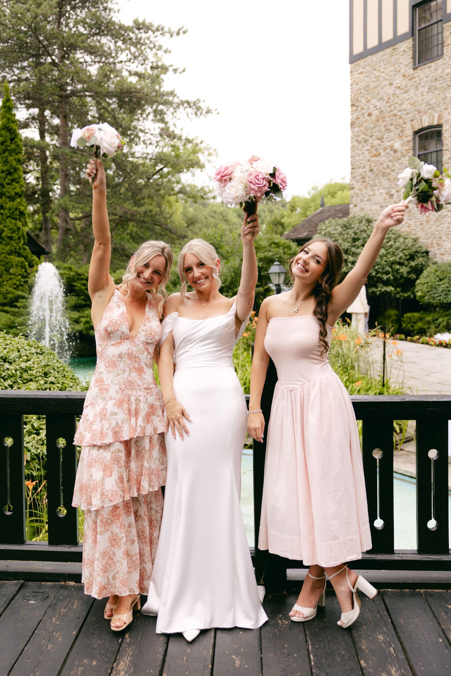 Wedding party in blush pink dresses posing playfully on a wooden deck.