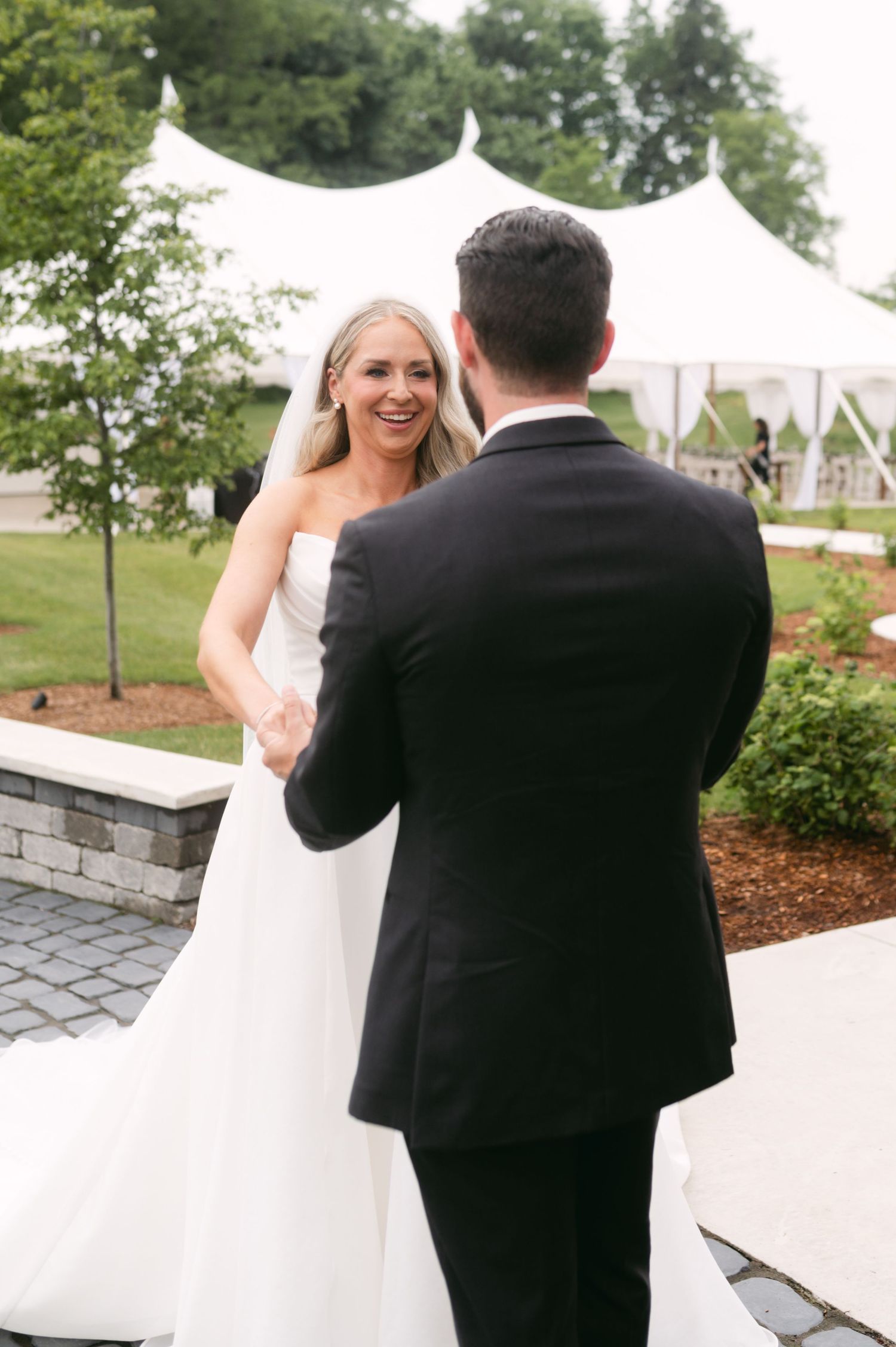 Couple shares first look moment on stone patio with white tent in background.