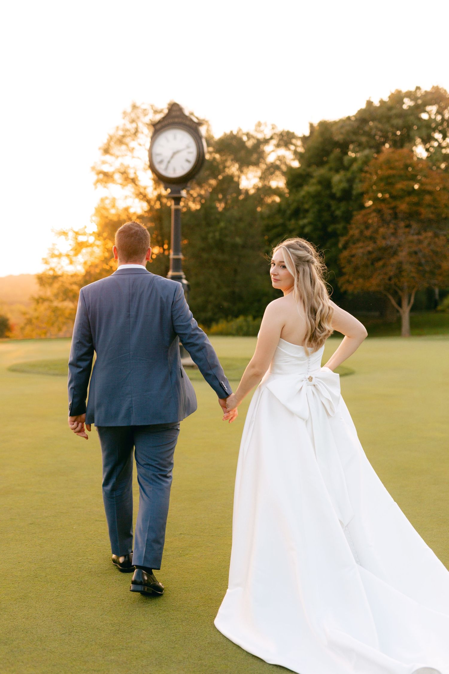A couple walks hand in hand across a scenic golf course during golden hour.