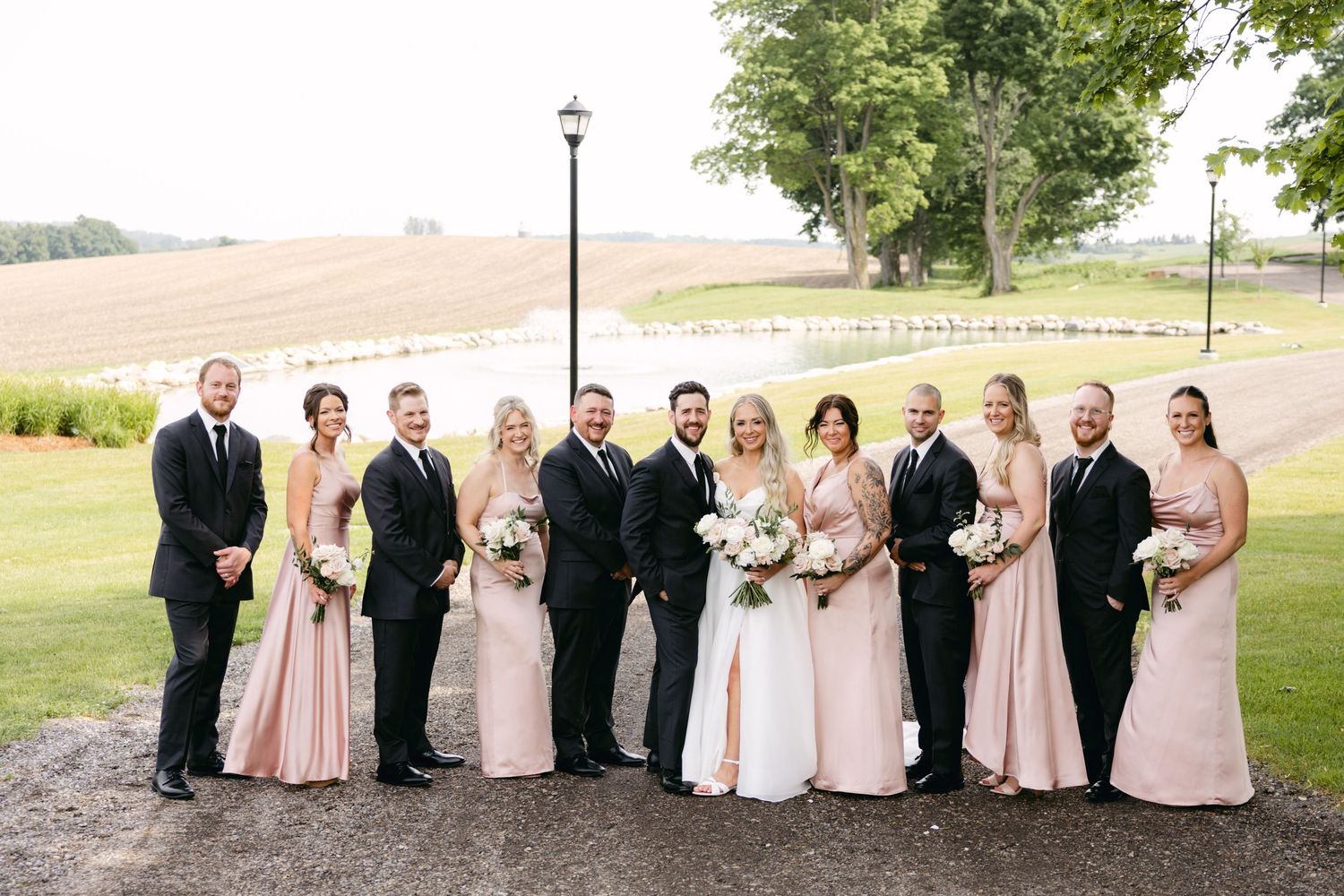 Wedding party members in pink dresses and black suits stand together on manicured grounds.