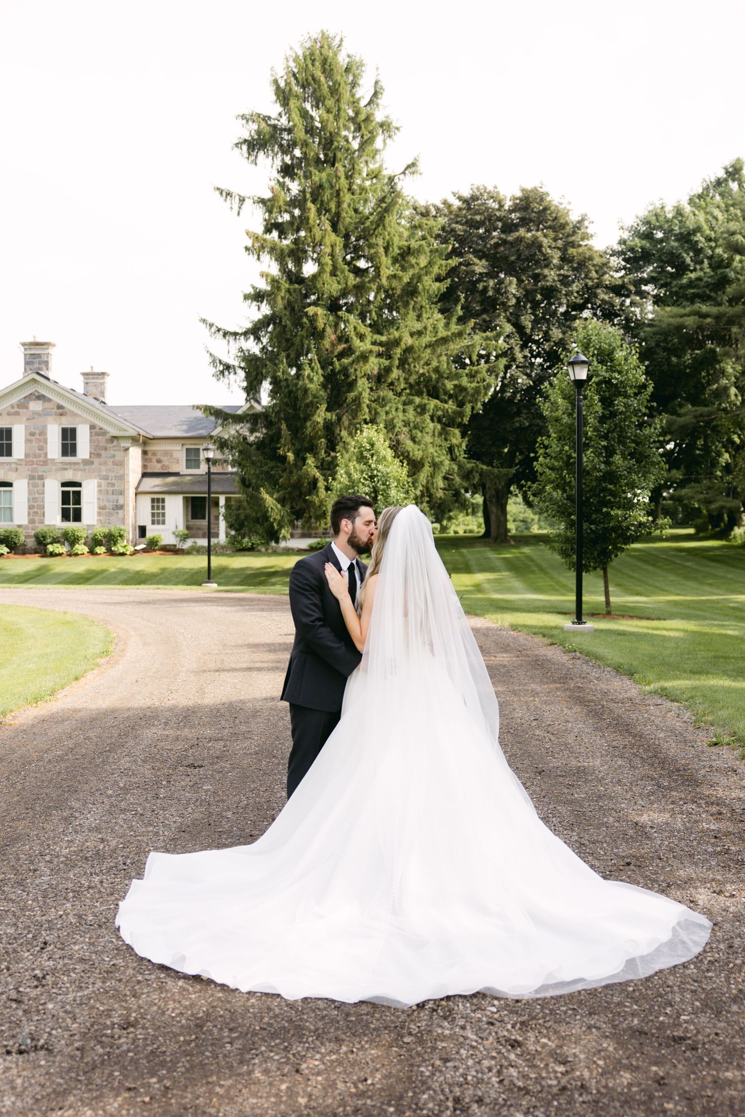 A romantic wedding photo showcasing the bride's dramatic cathedral-length train against a historic mansion backdrop.
