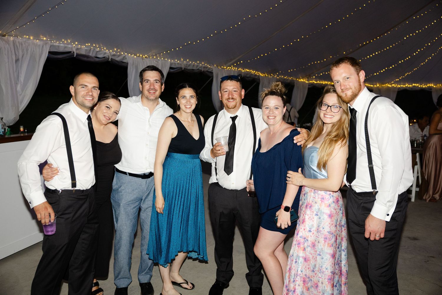 Wedding reception guests dance and celebrate under string lights at night.