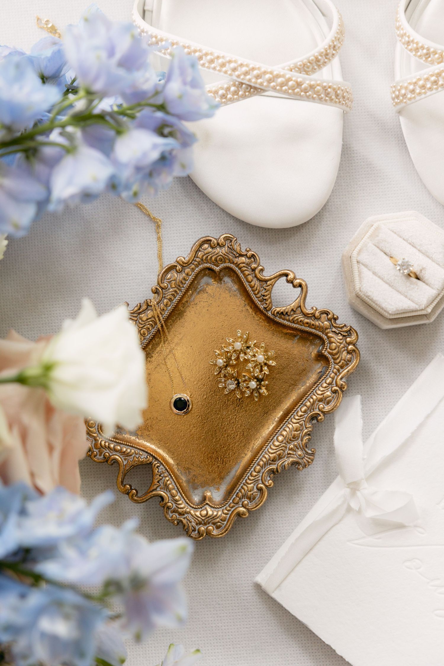 Vintage gold jewelry tray with ornate details displayed with soft blue flowers and white ribbons.