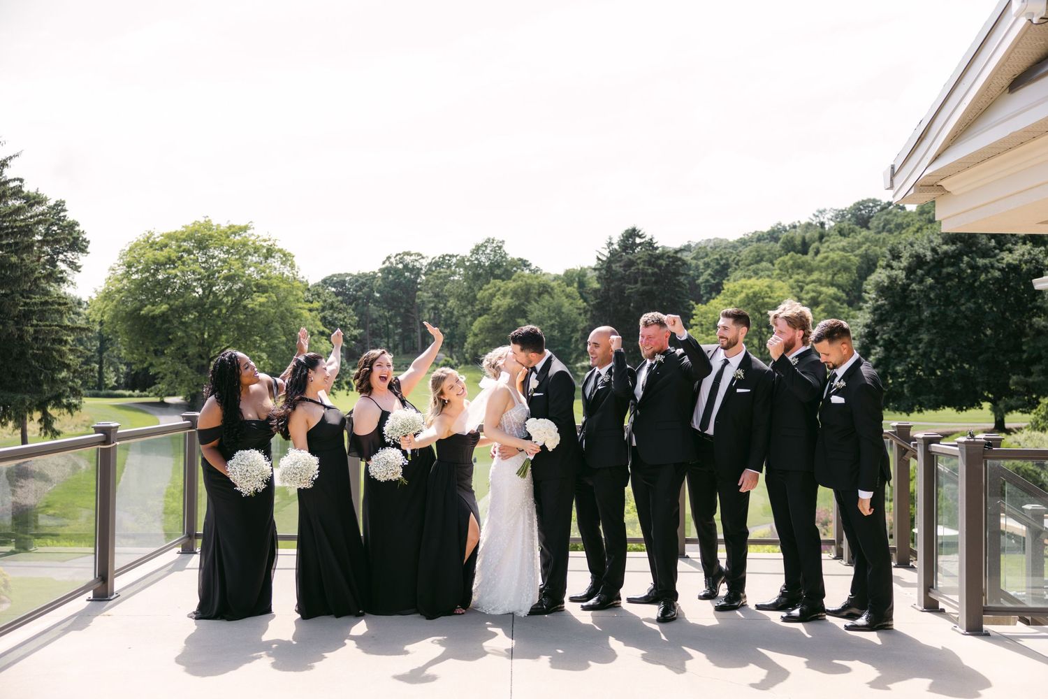 Wedding party poses in line on outdoor venue patio wearing formal black and white attire.