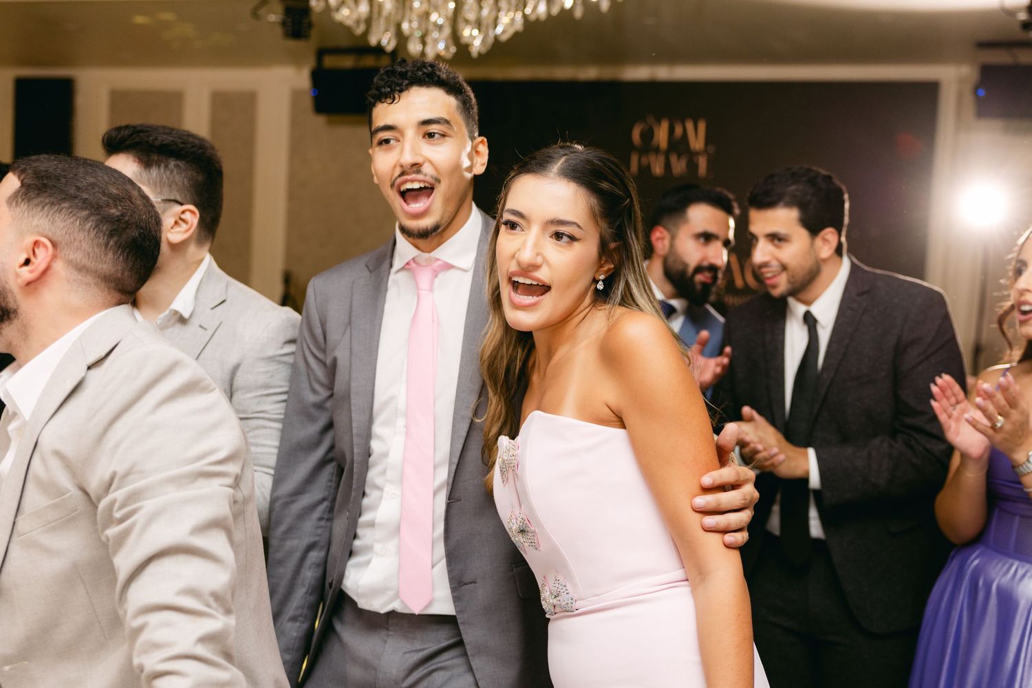 Wedding guests celebrate joyfully on the dance floor during a reception.