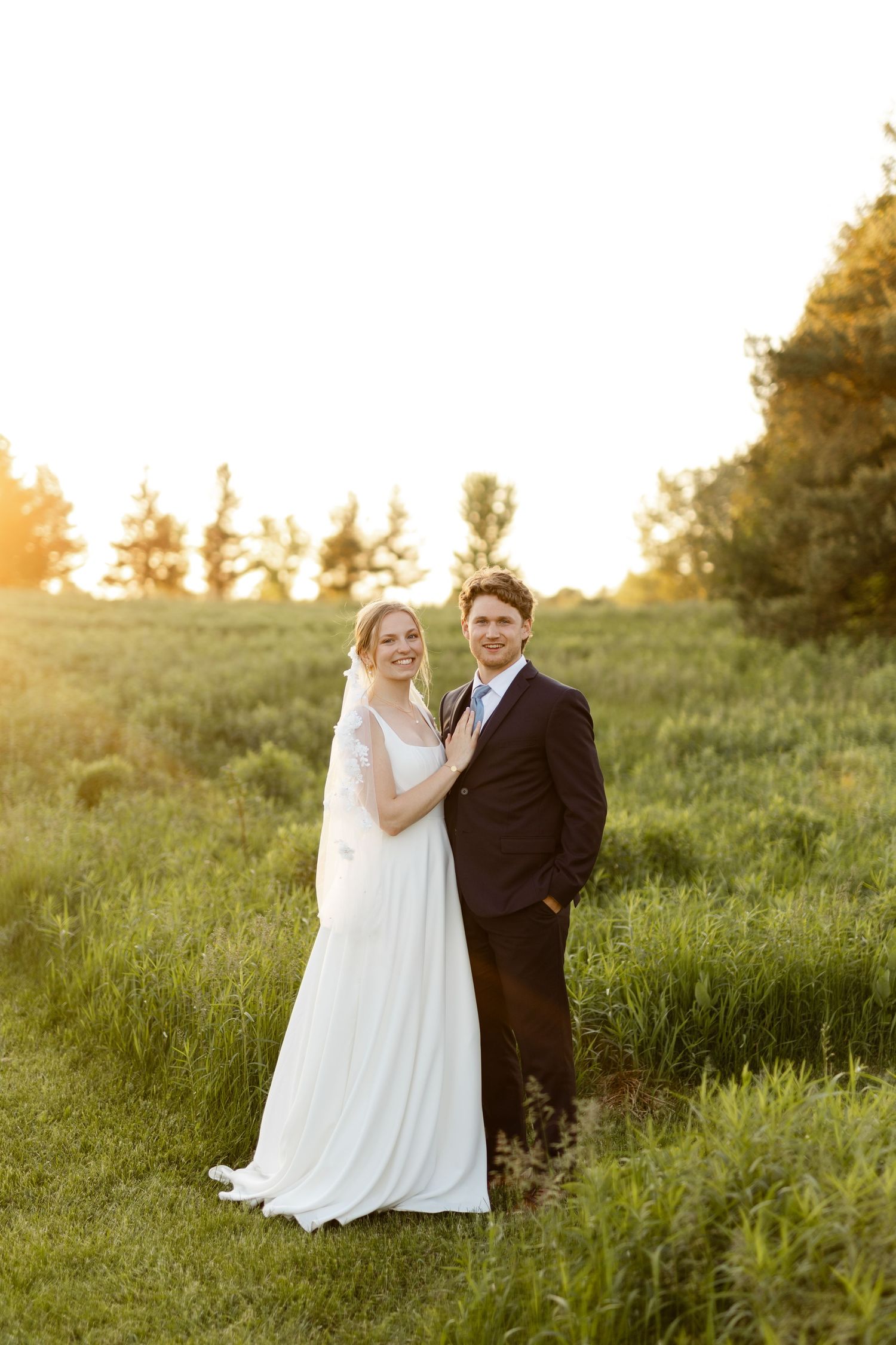A bride and groom share an intimate moment in a grassy field during golden hour.
