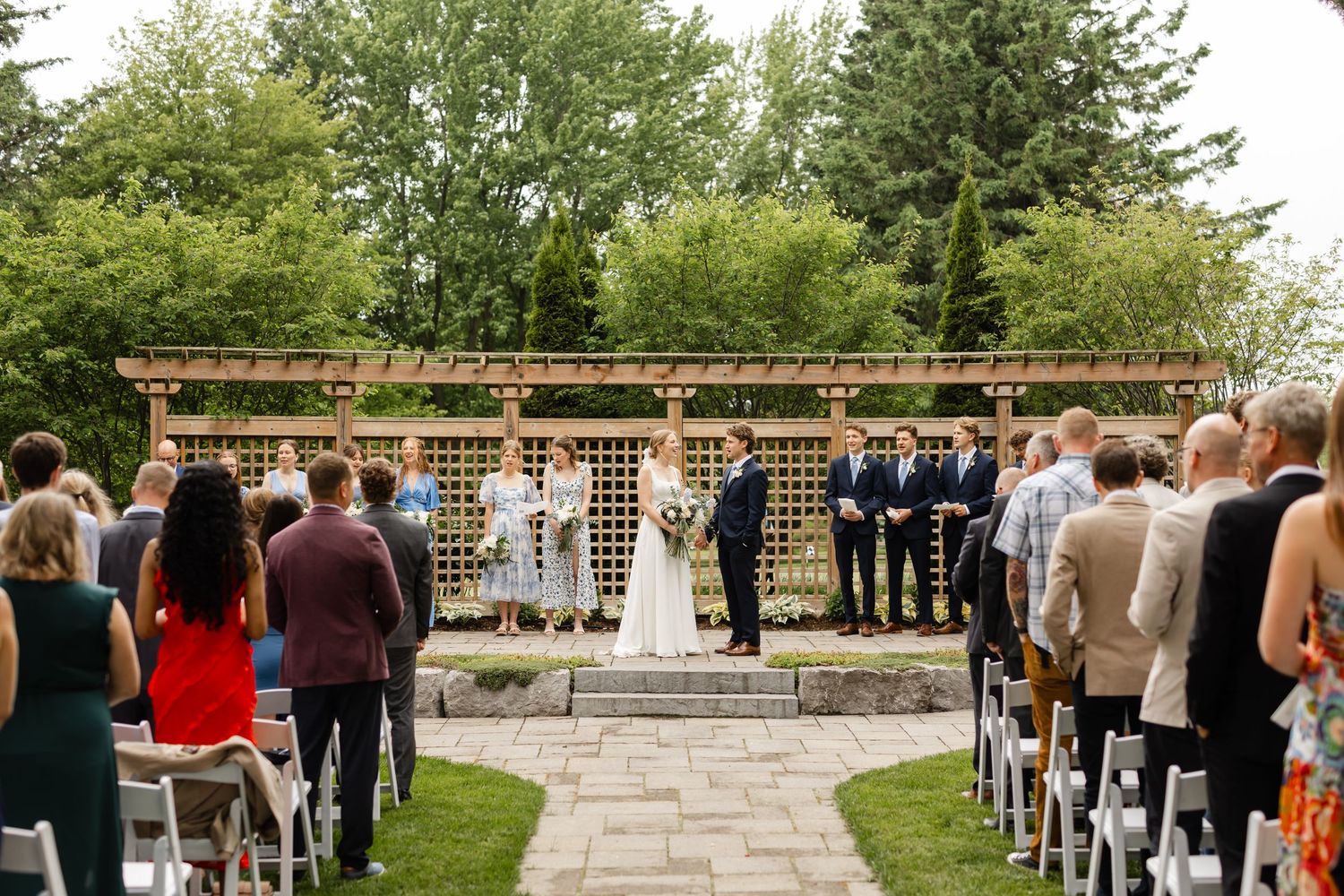 Garden wedding ceremony with guests seated facing wooden pergola and stone pathway.