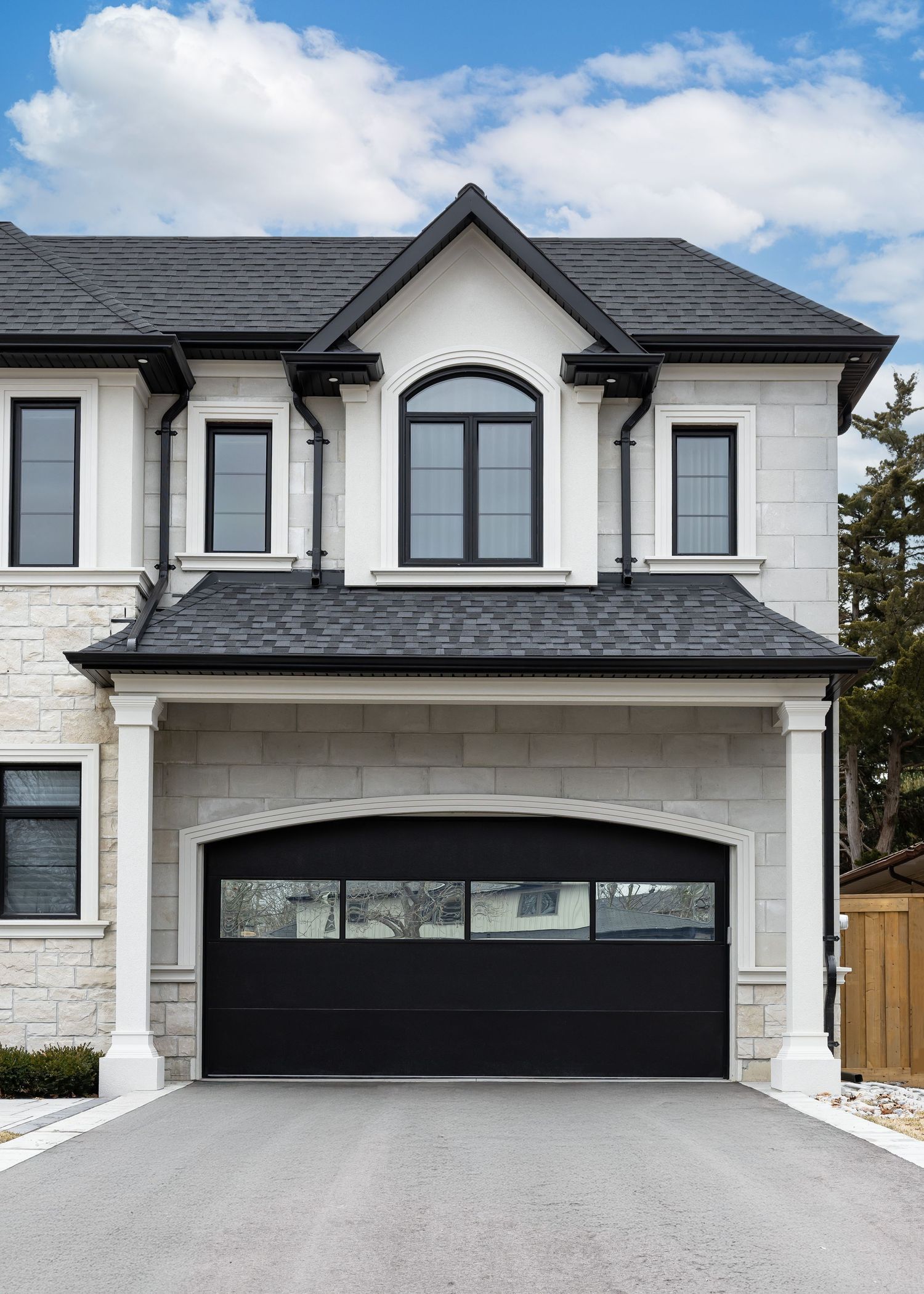 Modern stone house exterior with black garage door and architectural gable details.