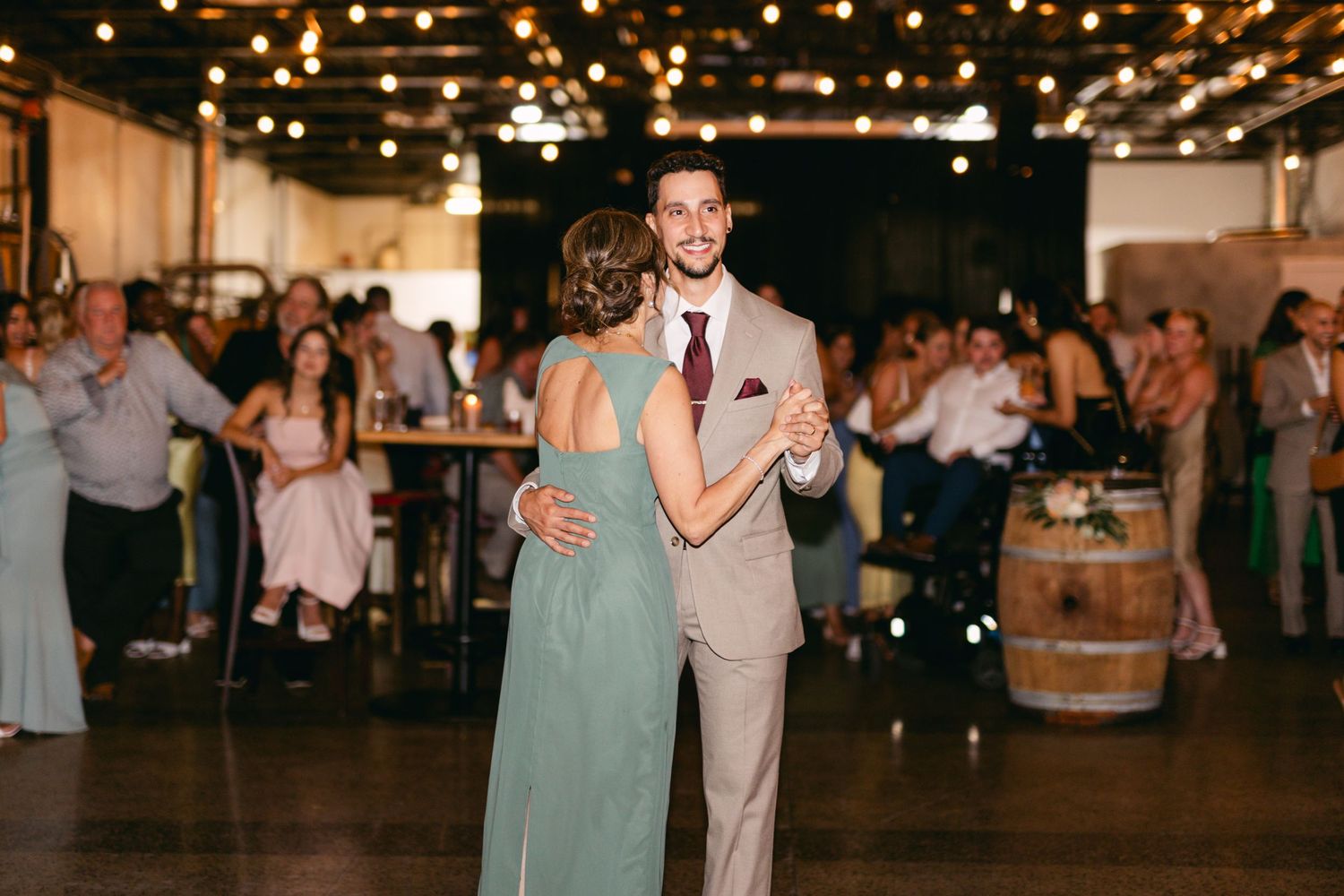 Wedding celebration with guests dancing under twinkling lights in rustic indoor venue.