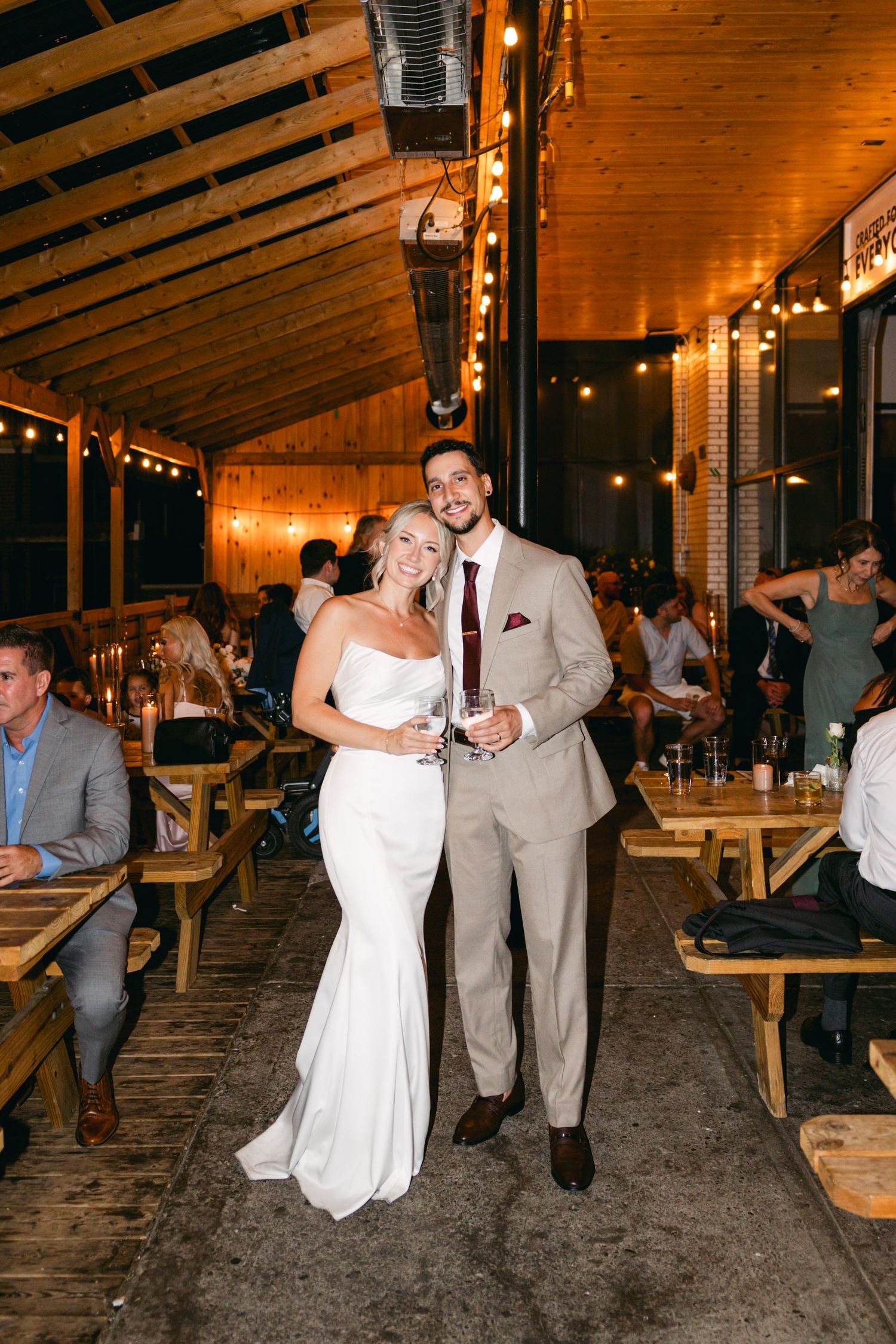 Couple walking through a rustic wooden venue decorated with string lights.